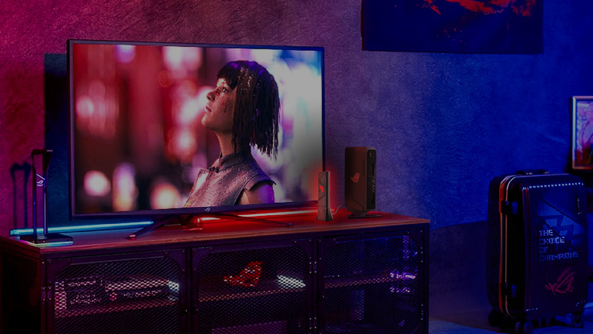 Schermo TV con volto di donna, dispositivi ROG su un mobile in legno e una valigia. La scena ha uno schema di colori rosso e blu.
