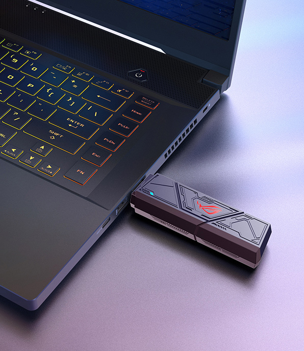 Un laptop con tastiera retroilluminata è collegato a un disco rigido esterno ROG. La scena è su una superficie scura.