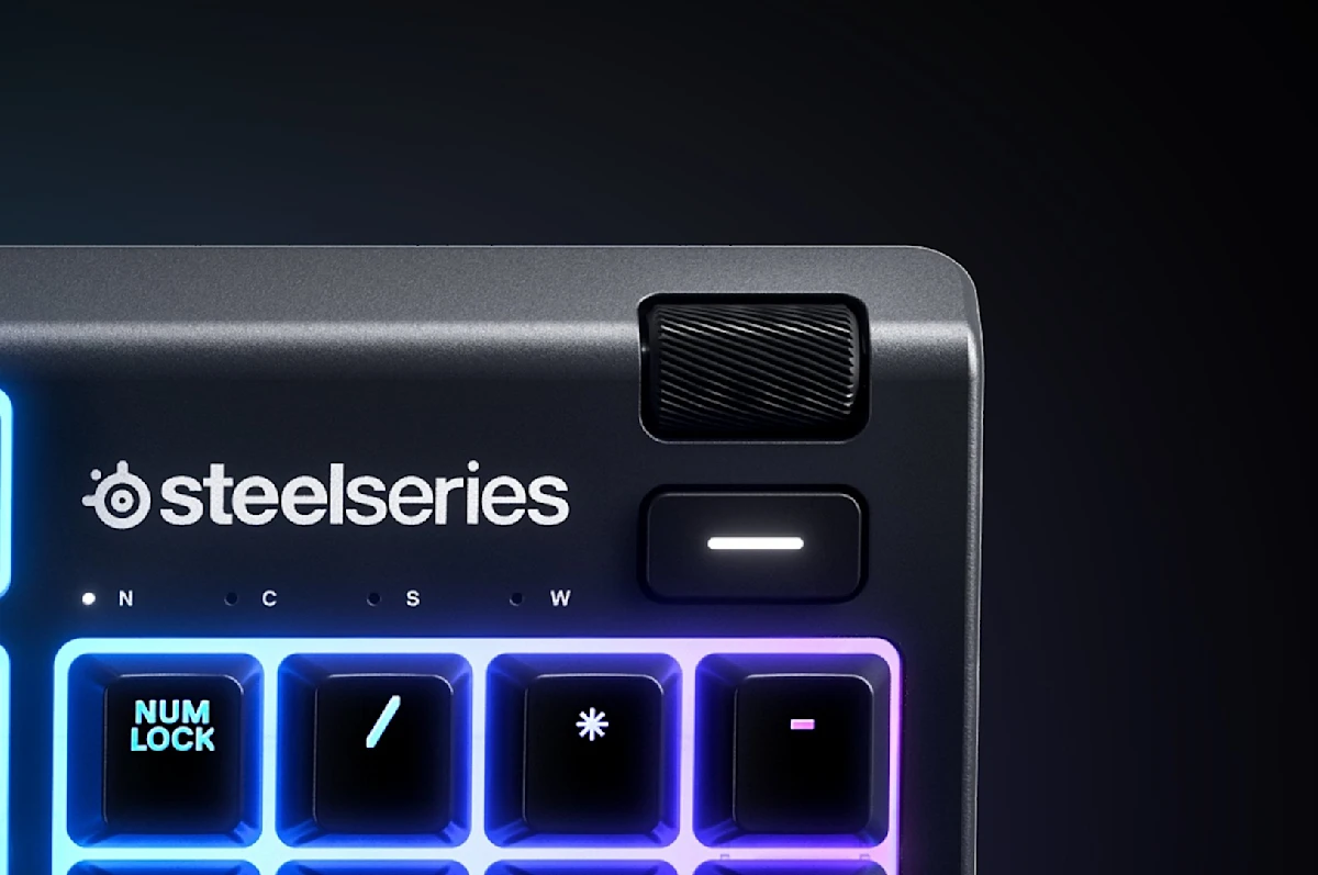 Nahaufnahme einer schwarzen SteelSeries-Tastatur. Sie hat beleuchtete Tasten, ein Lautstärkerad und das SteelSeries-Logo. Der Hintergrund ist dunkel.