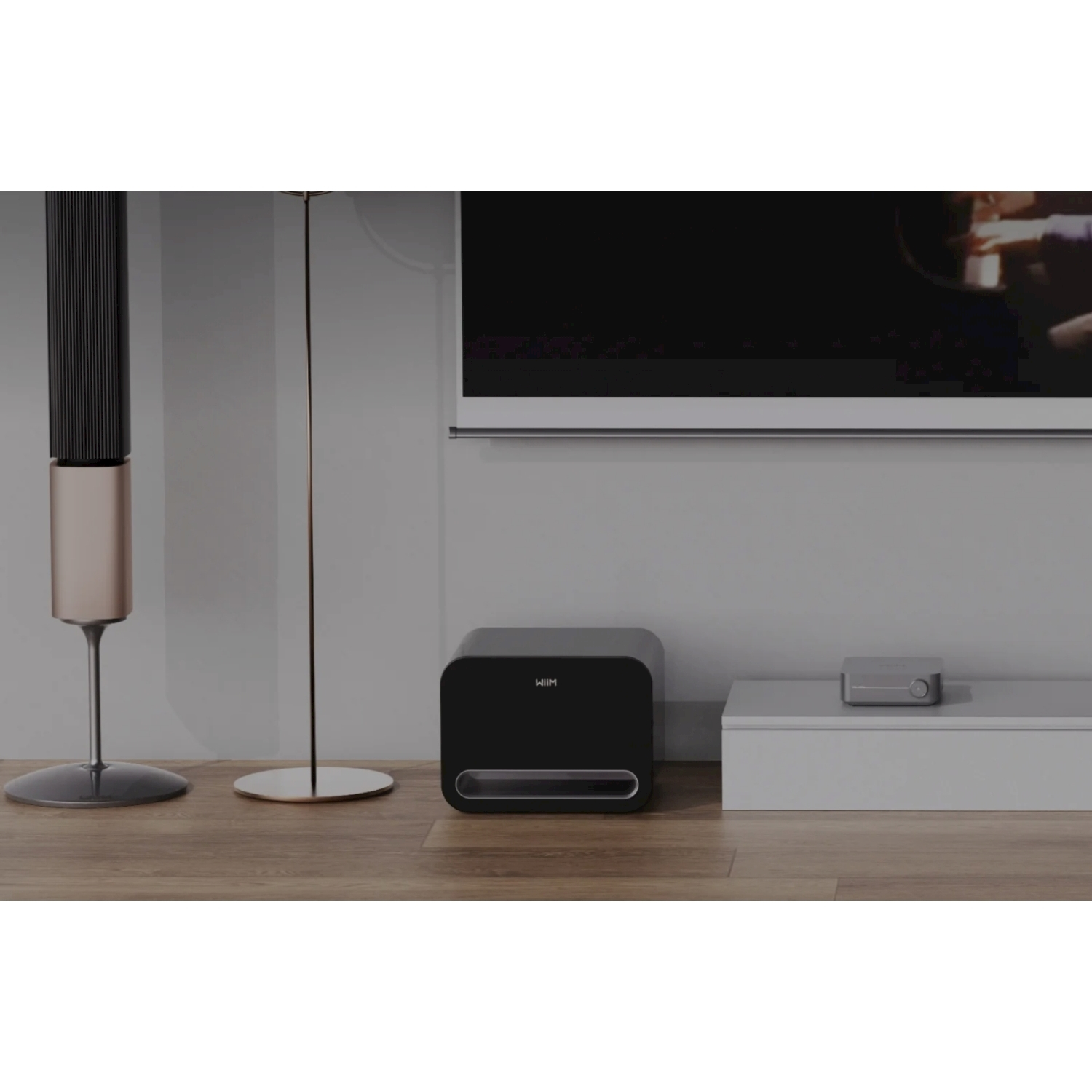 Un moderno soggiorno con un subwoofer nero, un altoparlante alto, una lampada, una TV e un mobile basso grigio chiaro su un pavimento in legno.