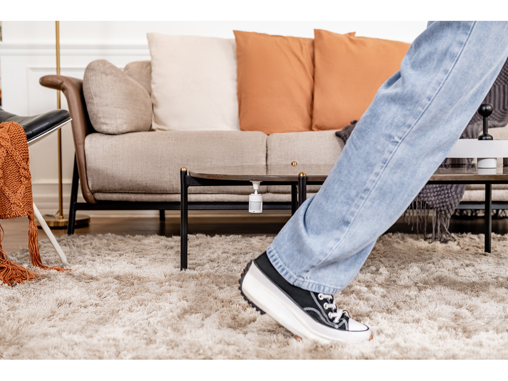 Eine Person in Jeans und Sneakers steht in der Nähe eines Couchtisches und eines Sofas mit orangefarbenen und beigen Kissen.
