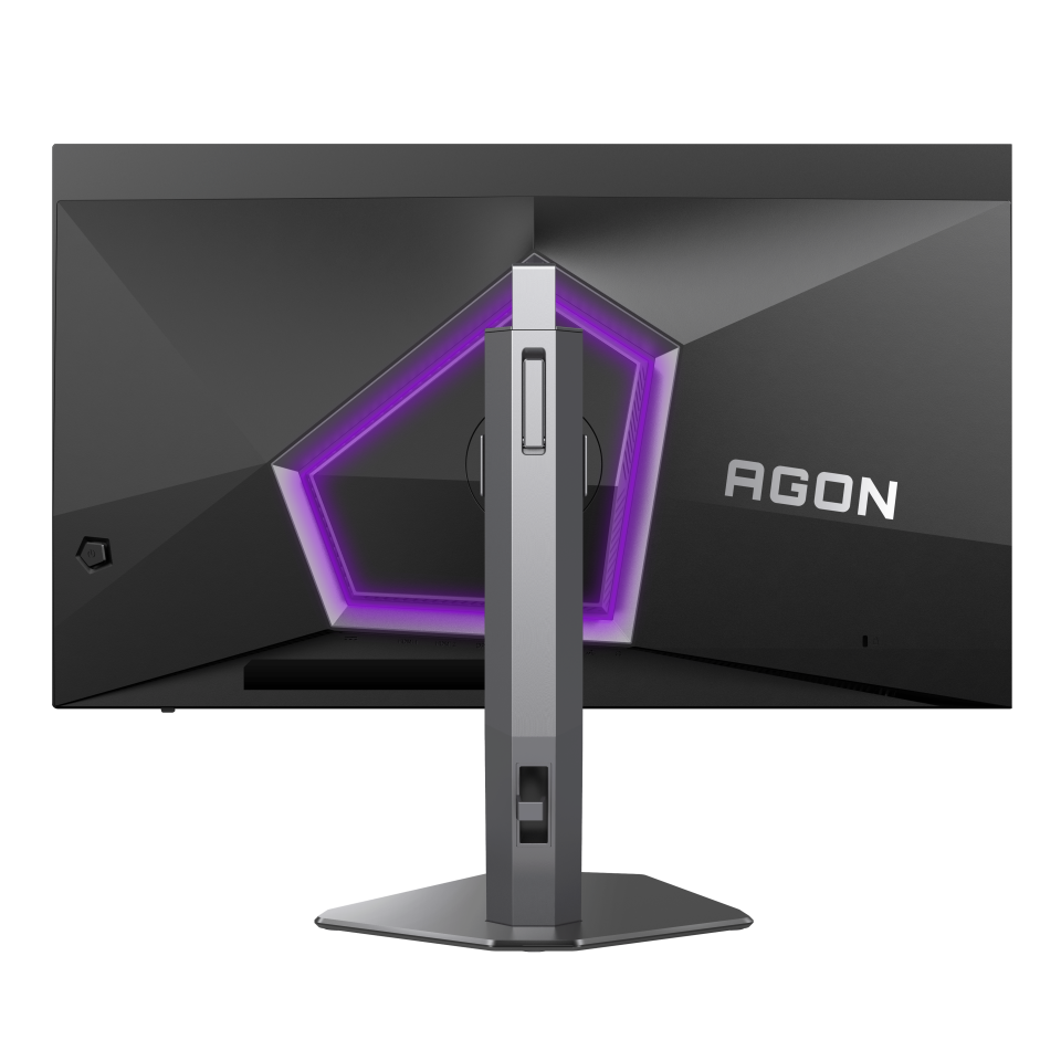 Egy fekete gamer monitor hátulja. Geometrikus kialakítású, lila világítással, és AGON felirattal. Szürke állványon áll.
