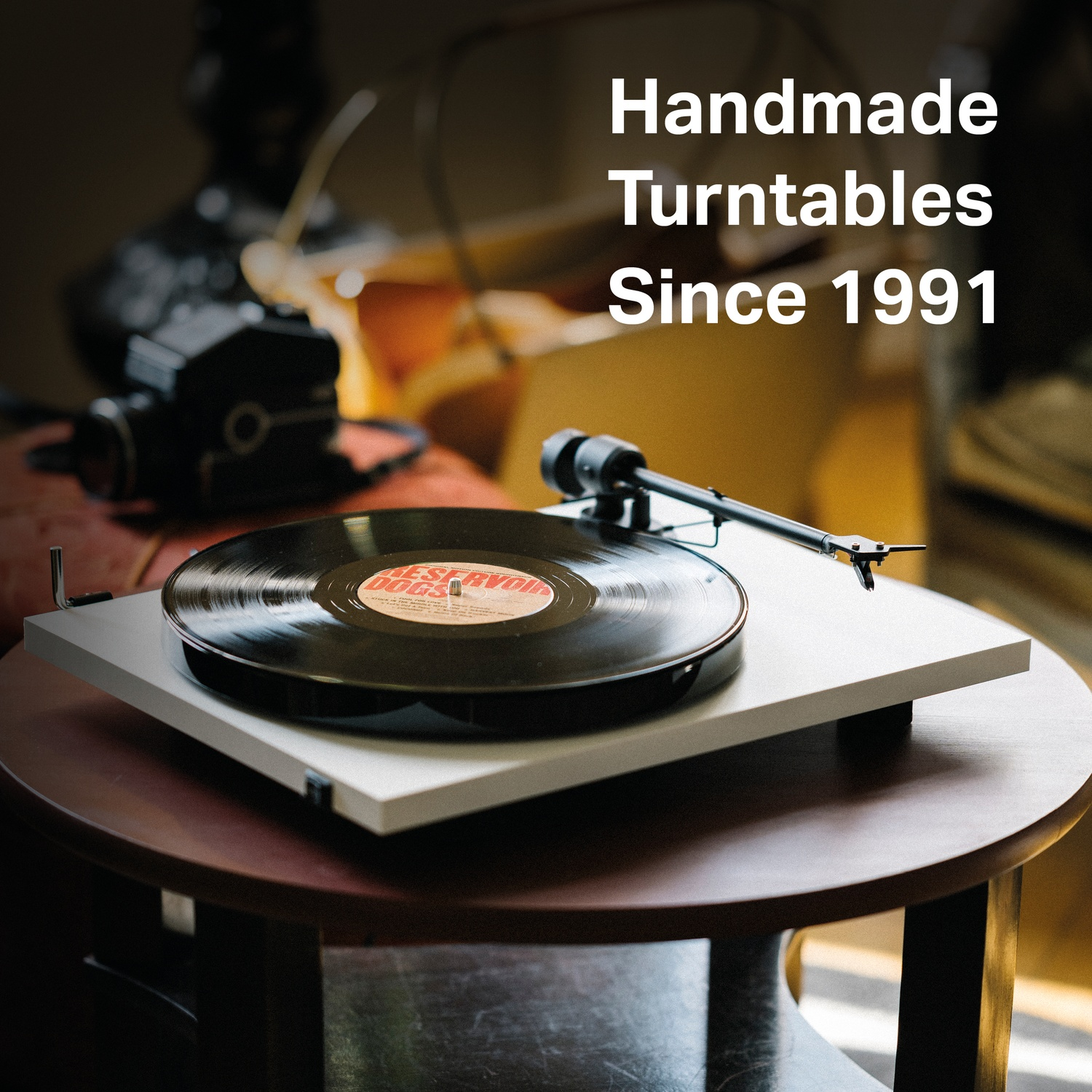 Un giradischi con un vinile su un tavolo rotondo. Testo: 'Handmade Turntables Since 1991'.