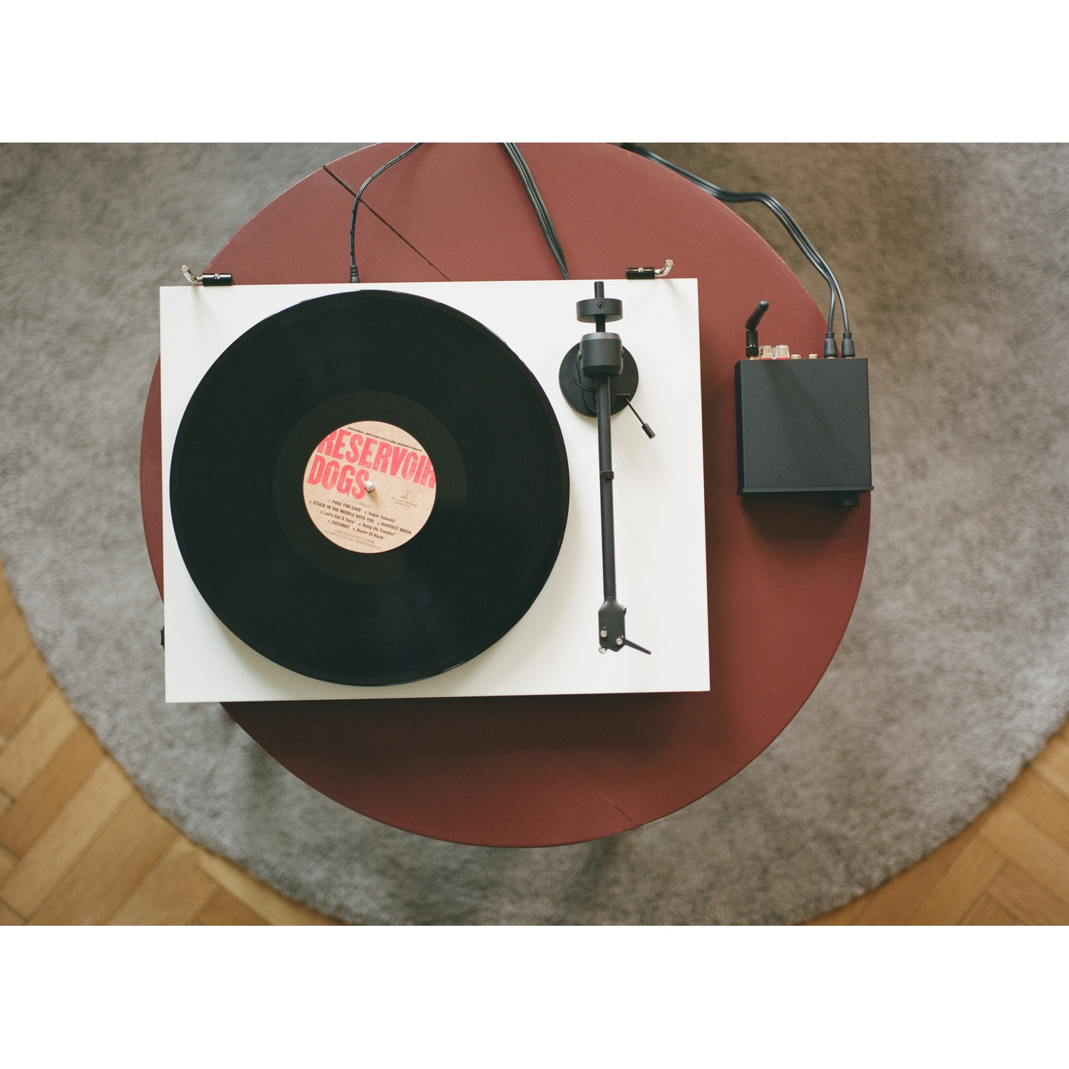 Un giradischi con un disco in riproduzione su un tavolo rosso. Una scatola nera è accanto. Il disco è etichettato 'Reservoir Dogs'.