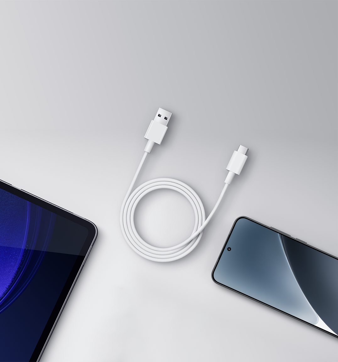 Fehér USB-C kábel, amely egy táblagépet és egy telefont köt össze. A kábel fel van tekerve. A háttér sima fehér.