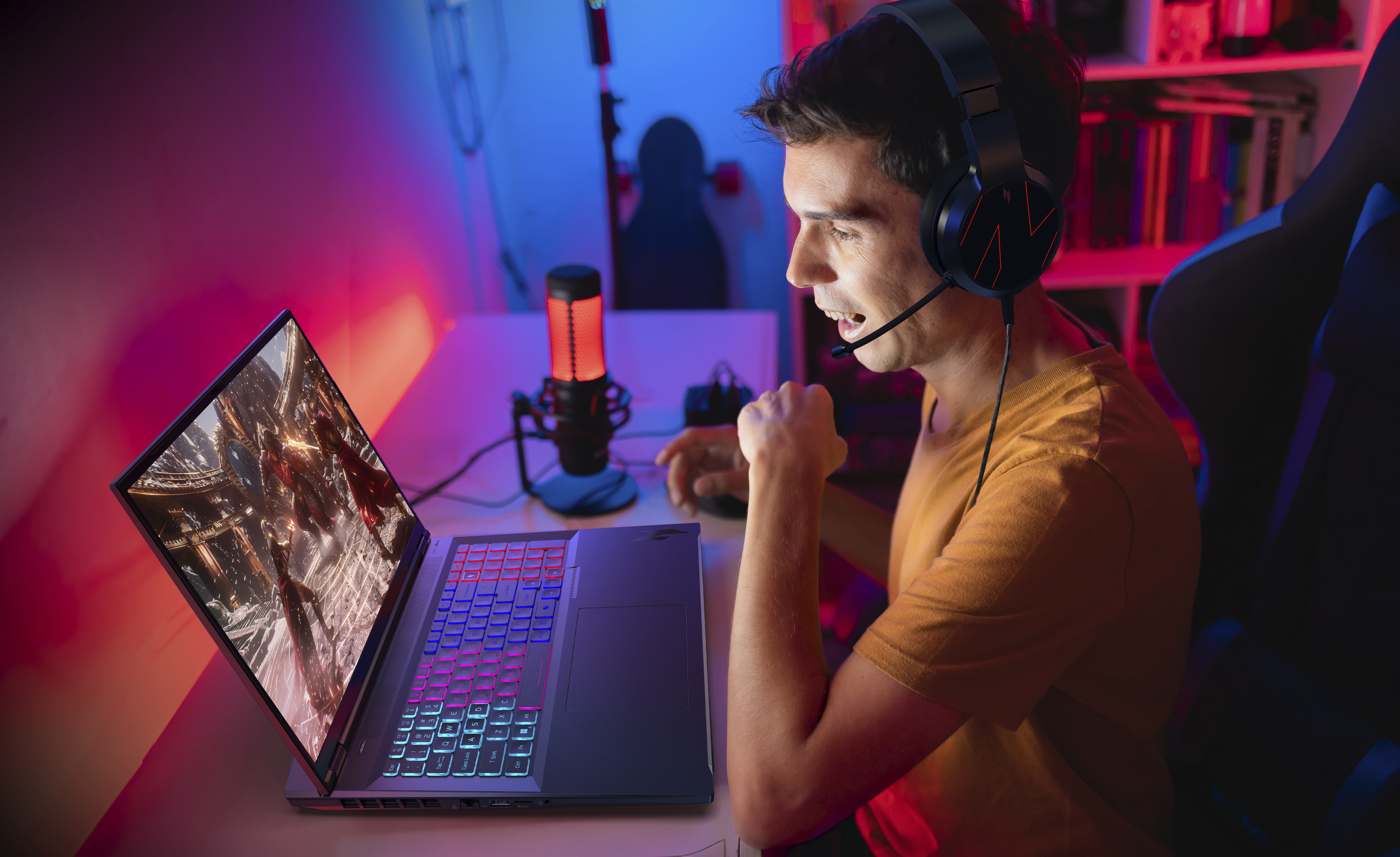 Ein Mann spielt mit Headset auf einem Laptop. Der Laptop zeigt eine Spielszene. Rotes und blaues Licht beleuchten den Raum.