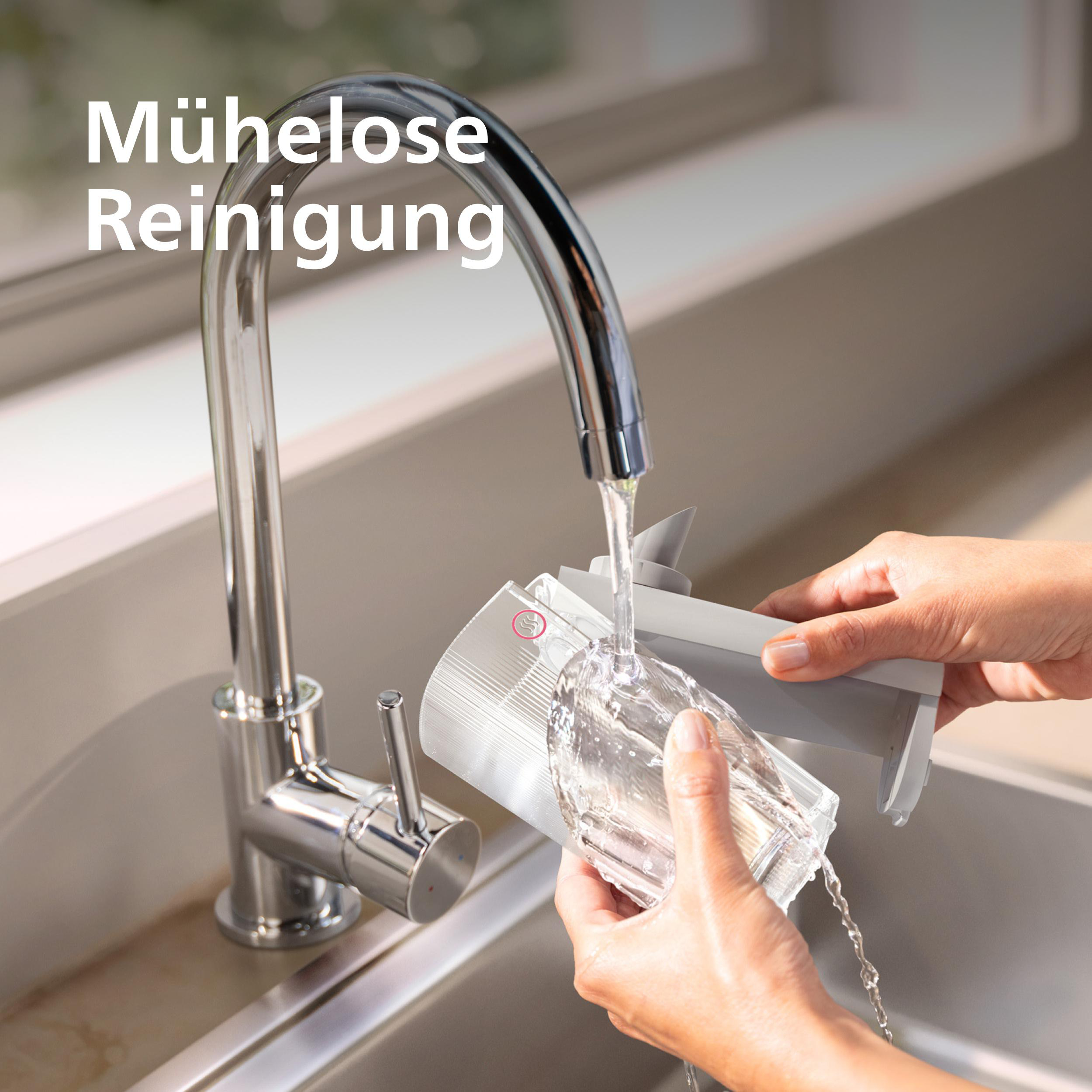Eine Person spült eine Glaskomponente unter einem laufenden Wasserhahn in einem Küchenbecken ab. Das Wasser ist klar.