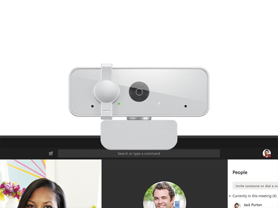 Eine Webcam befindet sich auf einem Bildschirm, der eine Videoanruf-Oberfläche anzeigt. Unten werden Teilnehmer und Chat-Optionen angezeigt.