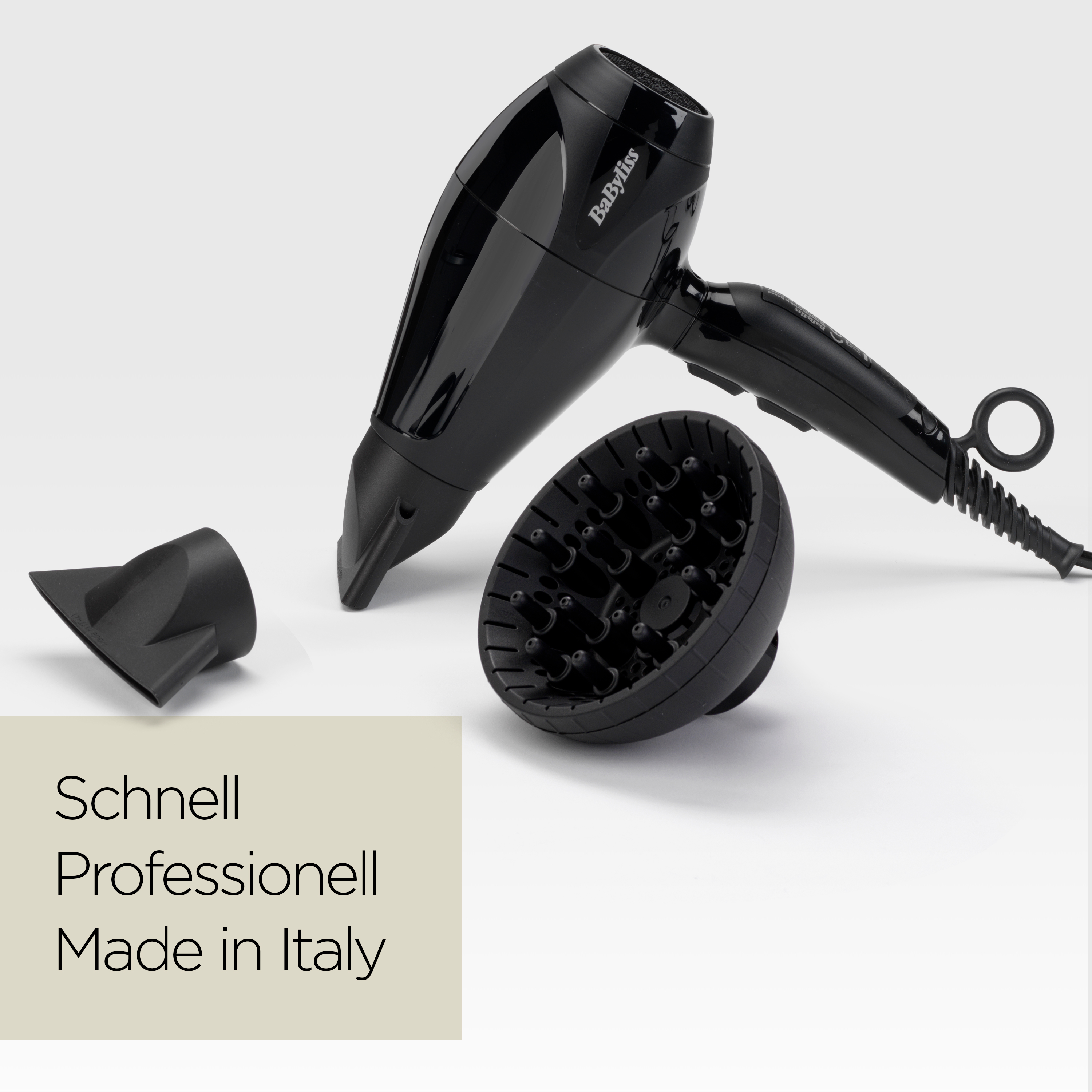 Ein schwarzer Babyliss-Haartrockner mit Aufsätzen liegt auf einer weißen Oberfläche. Text: 'Schnell Professionell Made in Italy'.