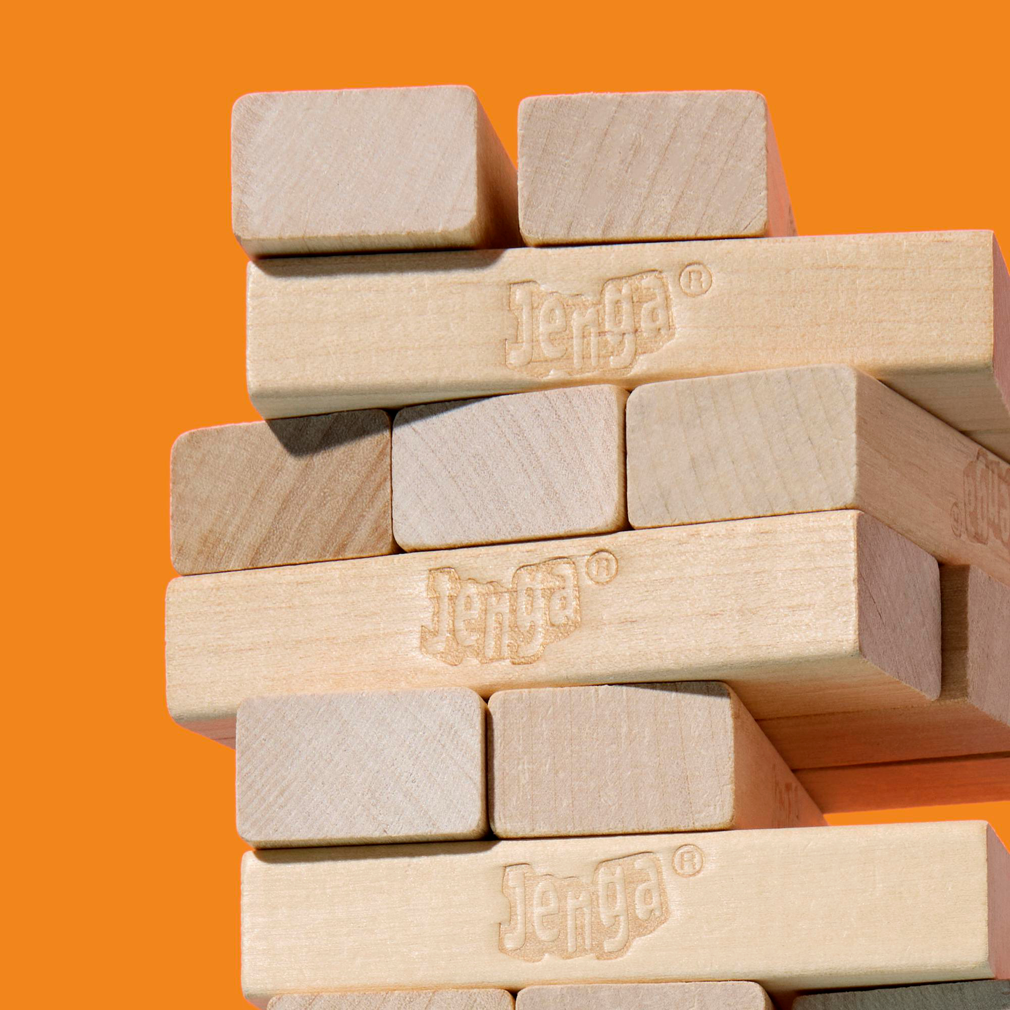Ein Jenga-Turm aus Holzblöcken mit dem Aufdruck 'Jenga' auf orangefarbenem Hintergrund.