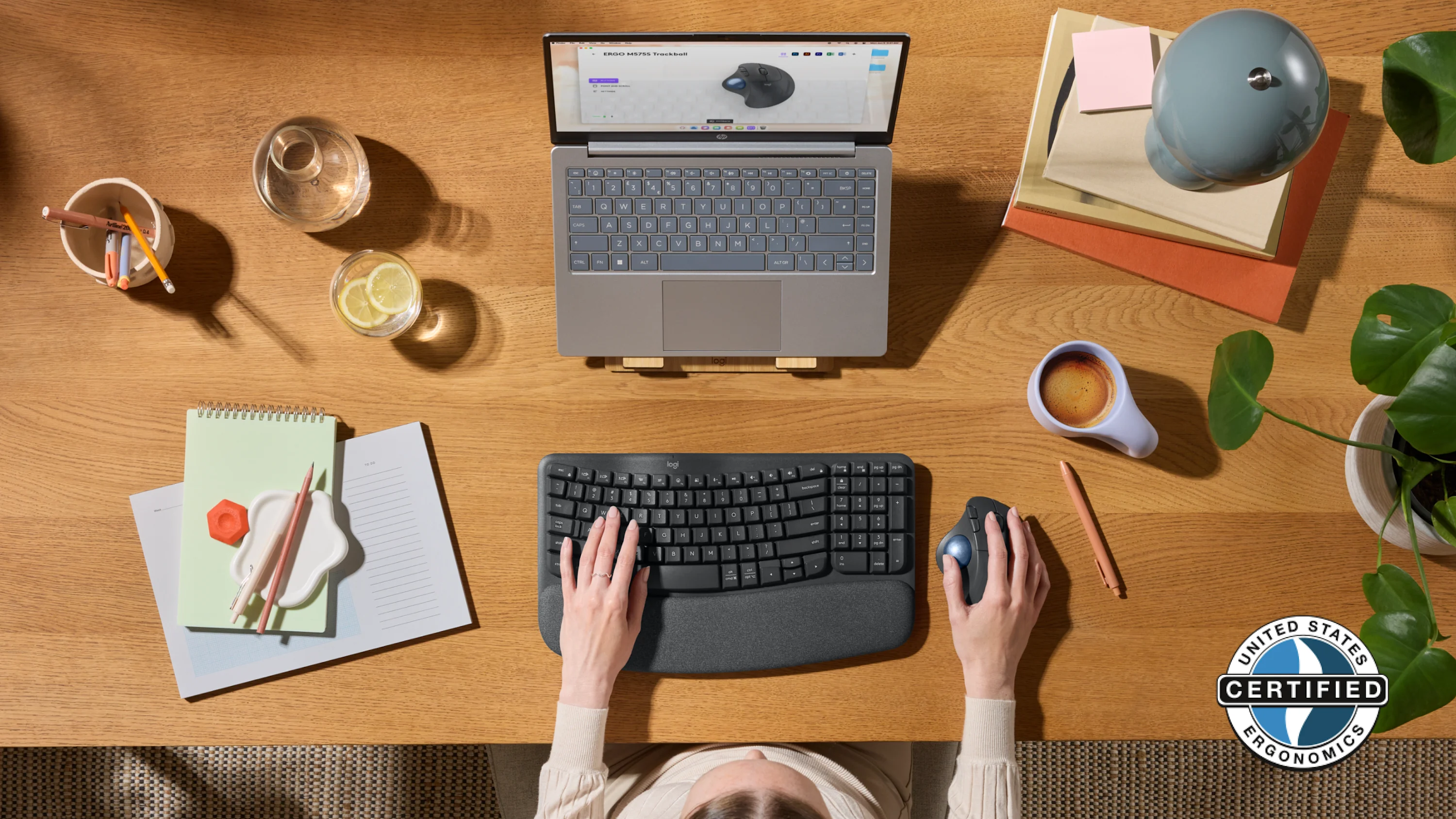 Un bureau avec un ordinateur portable, un clavier, une souris et diverses fournitures de bureau. Une personne utilise le clavier et la souris.