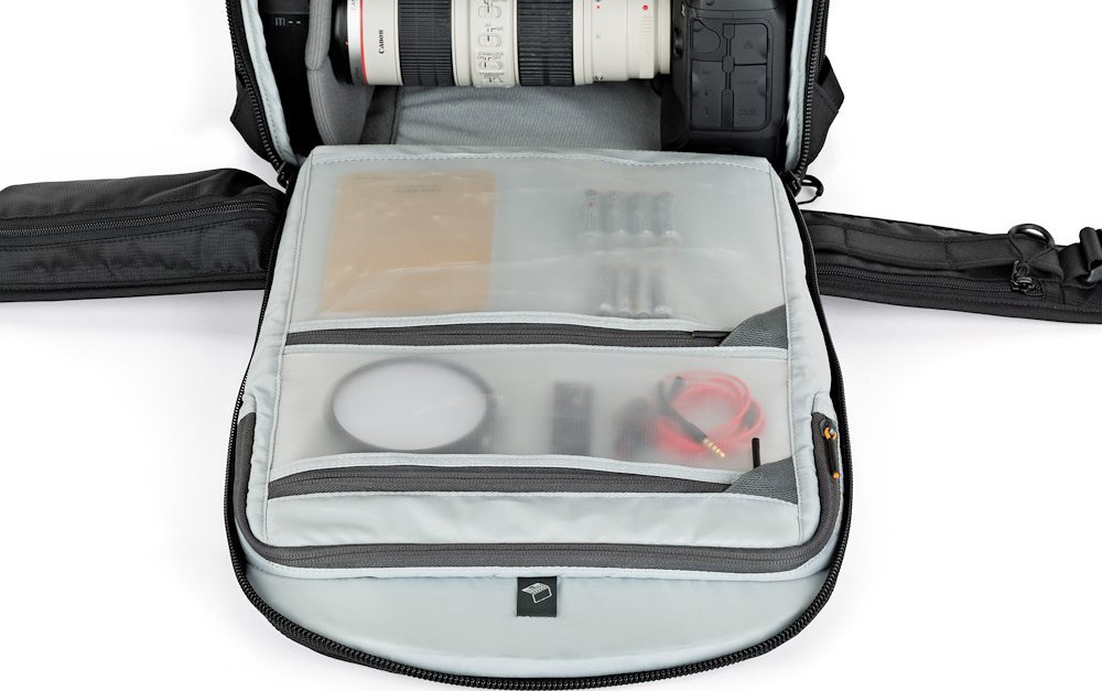 Una borsa nera per fotocamera è aperta, rivelando attrezzatura e accessori per fotocamera. Include un obiettivo, batterie, filtri e cavi.