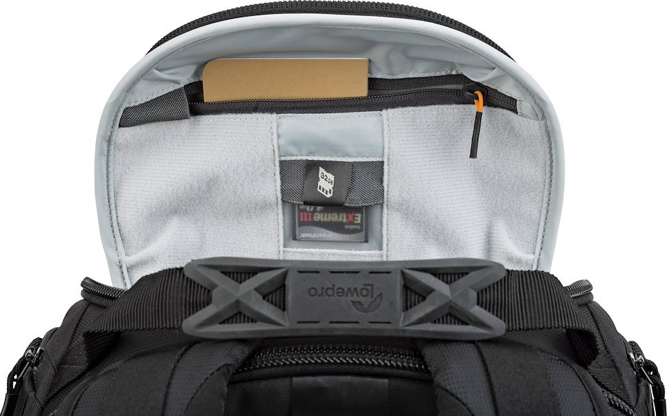 Una borsa per fotocamera Lowepro nera con interno grigio. Una carta è in una tasca superiore. La borsa ha una maniglia e una cerniera nere.
