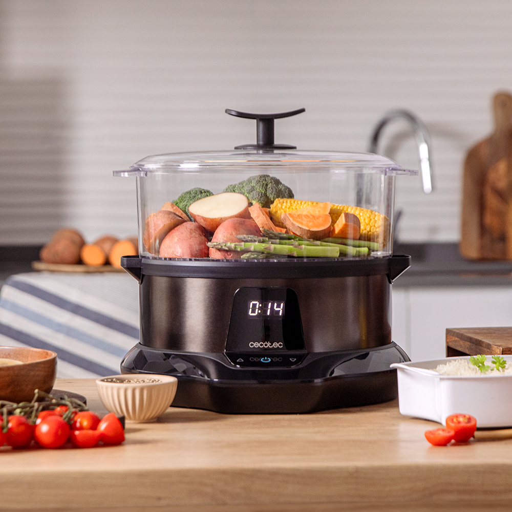 Una vaporera negra con verduras: patatas, maíz, brócoli, espárragos y batatas. Tomates y otros ingredientes están en la mesa.