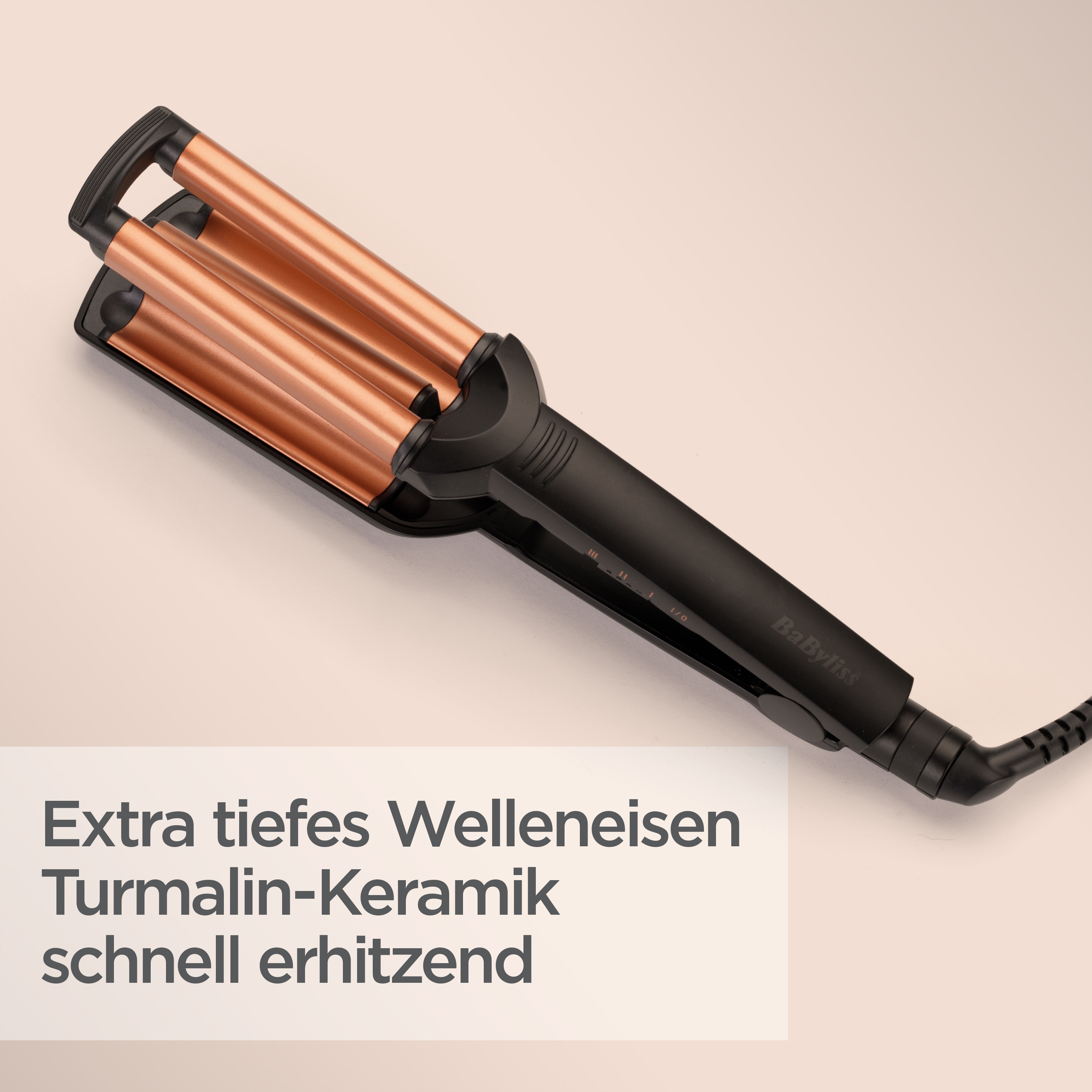 Ein schwarzer und kupferfarbener Haarweller auf einer beigefarbenen Oberfläche. Er hat drei Fässer und einen schwarzen Griff. Text unten.