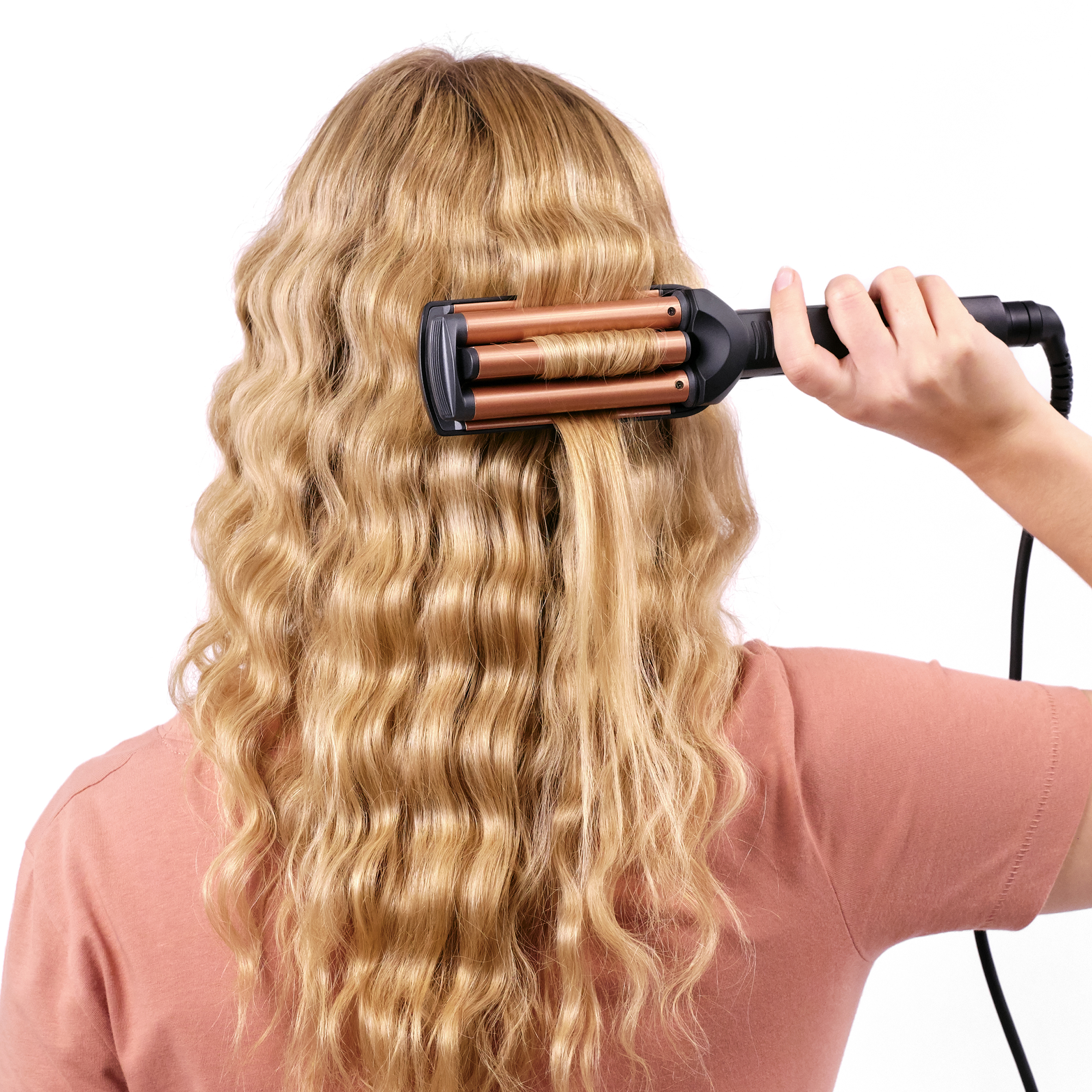 Blondes Haar wird mit einem Lockenstab gestylt. Die Person trägt ein pinkfarbenes Hemd und der Hintergrund ist weiß.