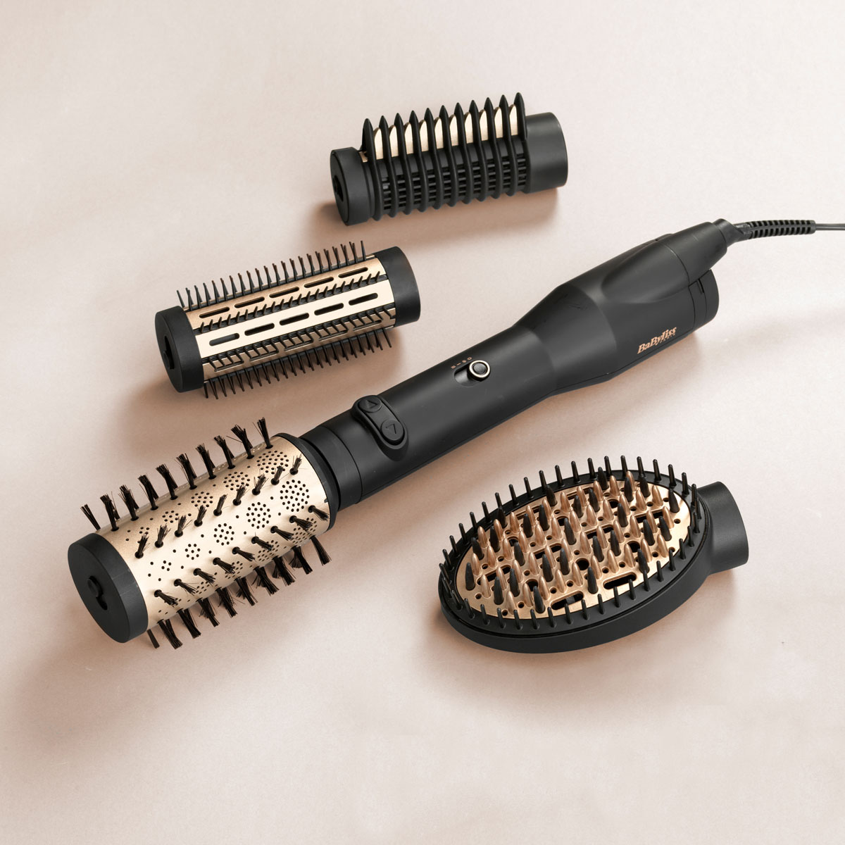 Ein schwarzes und goldenes BaByliss-Haarstyler-Set. Enthält den Hauptgriff und drei Bürstenaufsätze auf einer beigen Oberfläche.