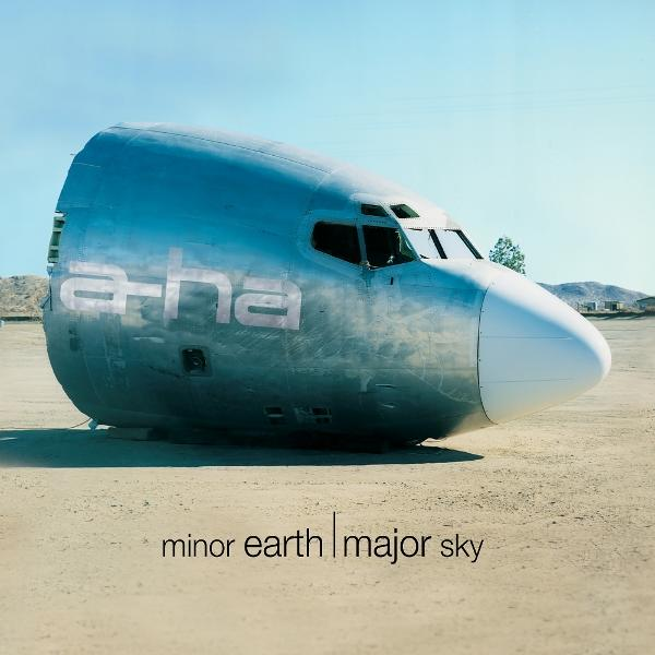 Die Nase eines Flugzeugs liegt auf Sand. Auf dem Rumpf steht a-ha. Albumtitel 'minor earth | major sky' steht darunter.