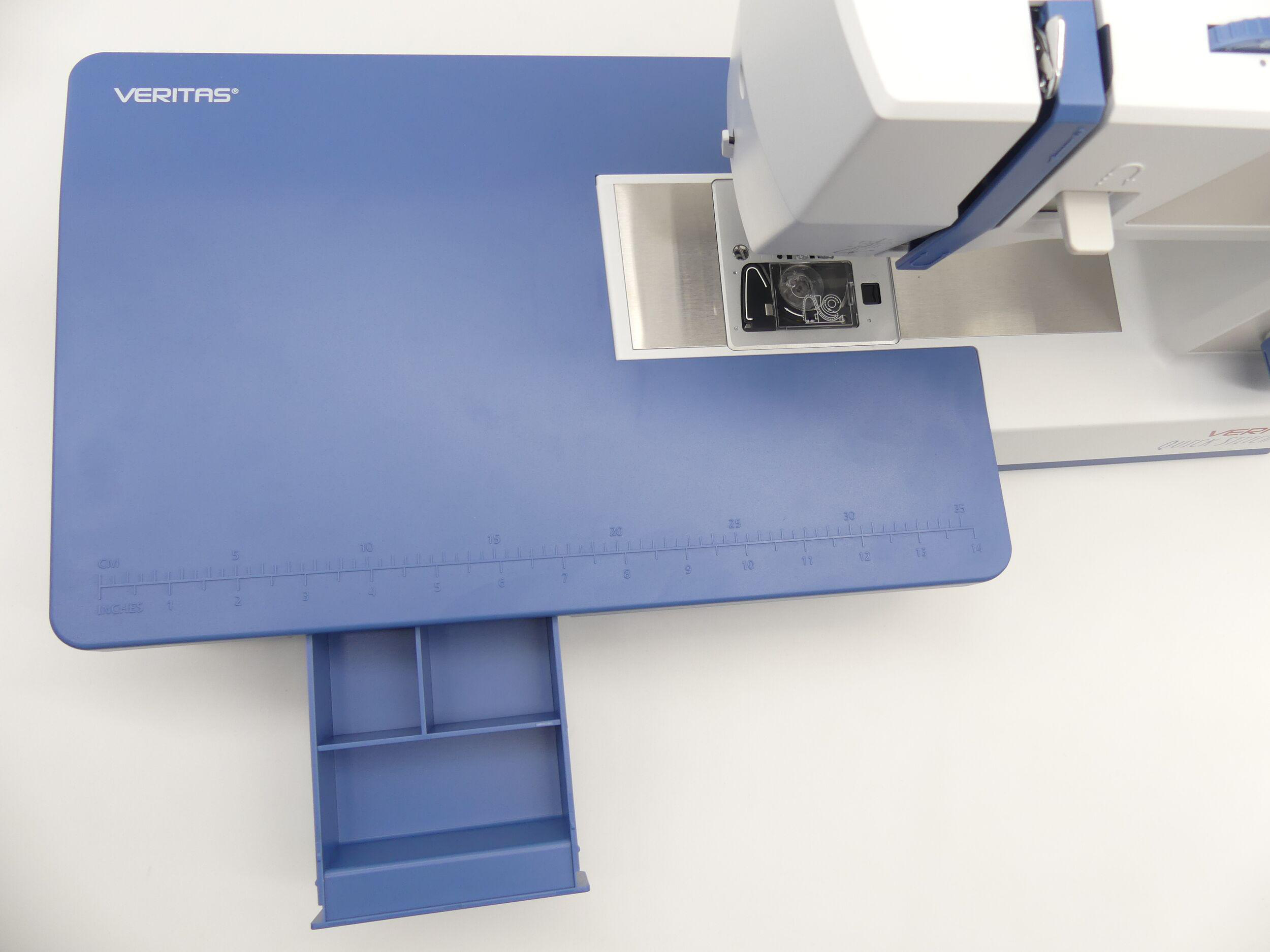 Eine Nähmaschine auf einer blauen Oberfläche mit Messmarkierungen und einer Schublade. Die Maschine ist weiß und blau.