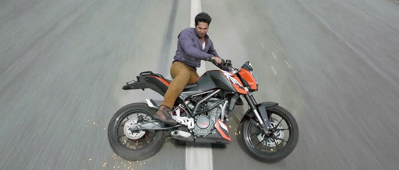 Ein Mann auf einem schwarz-orangenen Motorrad, mitten in einem Stunt auf einer Straße. Die Reifen des Motorrads wirbeln Funken auf. Asphalt-Hintergrund.