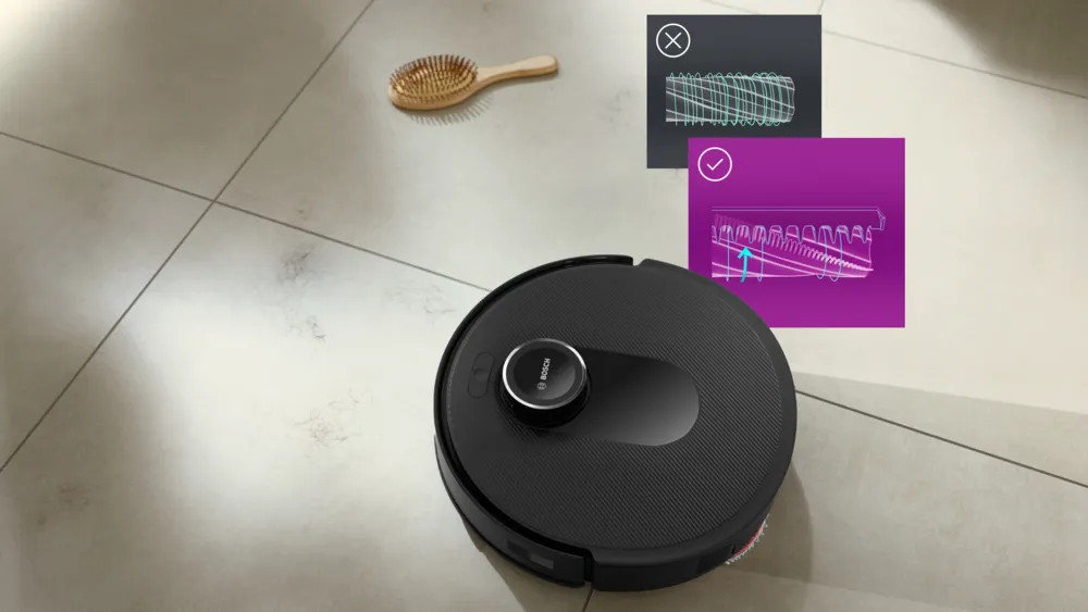 Czarny robot odkurzający na podłodze wyłożonej kafelkami. Obecna jest również drewniana szczotka i diagramy.
