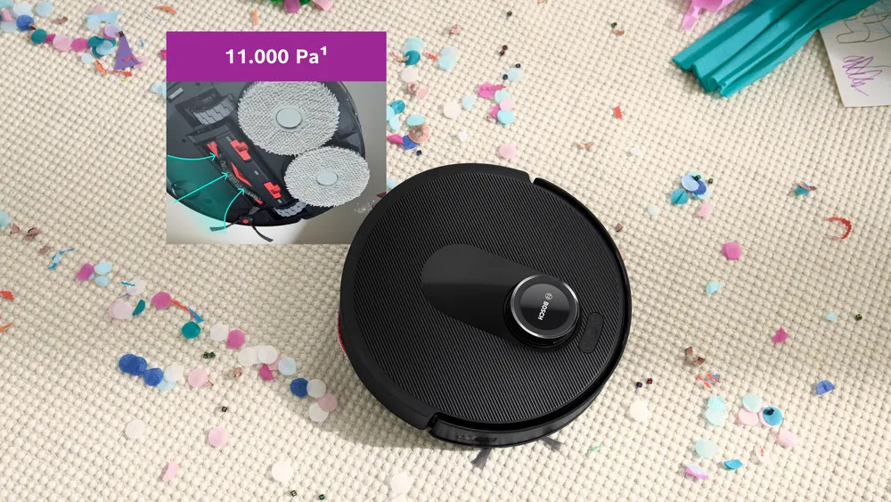 Czarny robot odkurzający na dywanie z konfetti, wstawka pokazująca elementy czyszczące odkurzacza.