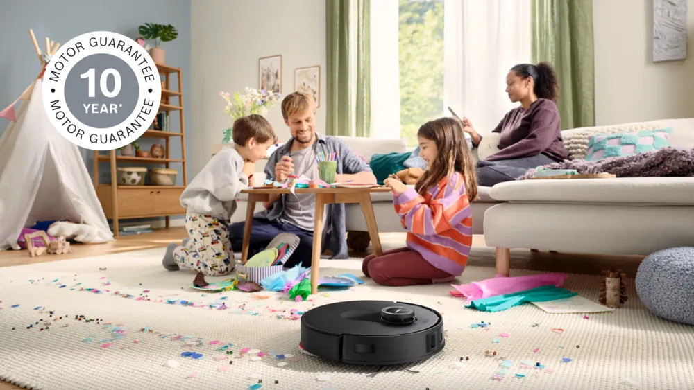 Rodzina tworzy rękodzieło na podłodze. Odkurzacz robot sprząta. Scena obejmuje sofę, tipi i logo 10-letniej gwarancji na silnik.