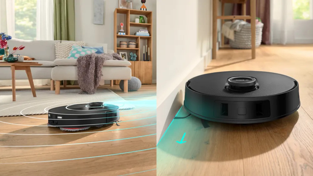 Czarny robot odkurzający na drewnianej podłodze. W tle salon. Robot sprząta.