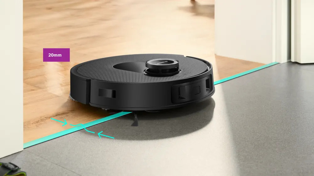 Czarny robot odkurzający na drewnianej podłodze, blisko drzwi. Fioletowe pole wskazuje szczelinę 20 mm.