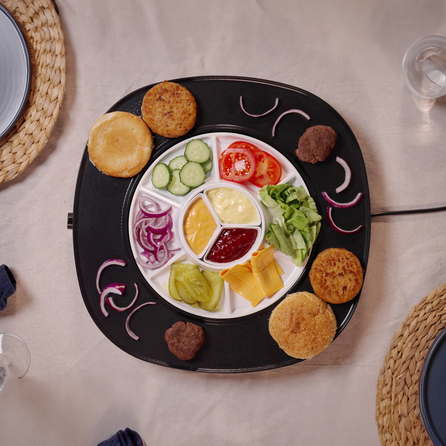 A divided plate with burger ingredients: buns, patties, cheese, pickles, tomatoes, lettuce, onions, and sauces.