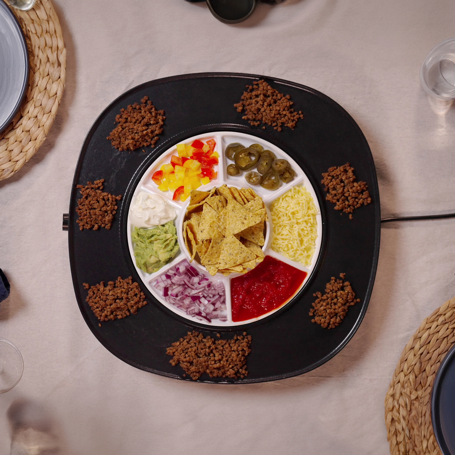 A circular tray with ingredients like ground meat, nachos, diced peppers, cheese, onions, and sauces for a taco night.