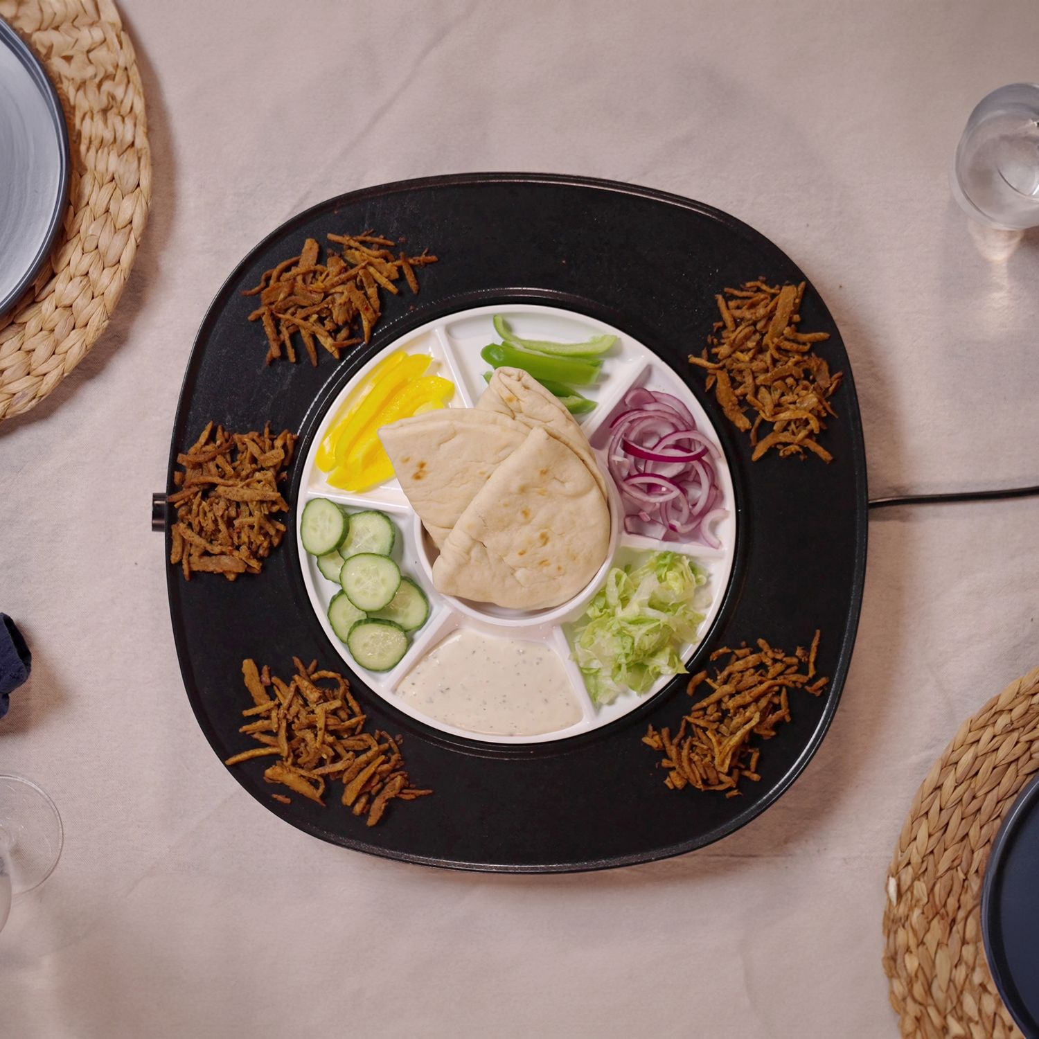 Overhead shot of a platter with various foods: pita bread, vegetables, sauce, and fried meat. Plates and glasses are visible.