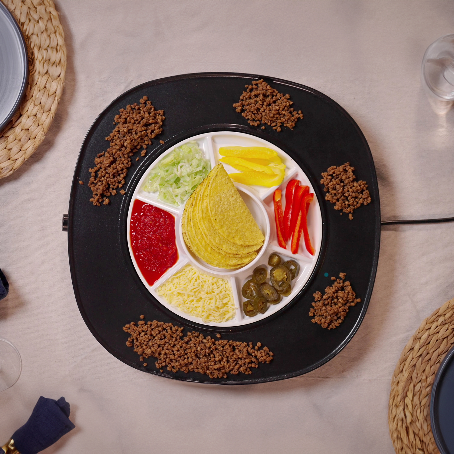Overhead view of a taco bar. It has meat, lettuce, tomatoes, cheese, peppers, jalapenos, and taco shells. Placed on a black plate.