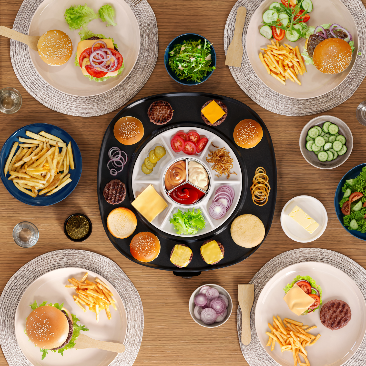Overhead shot of a table set for burgers. Plates with burgers, fries, and bowls of toppings surround a central burger component tray.