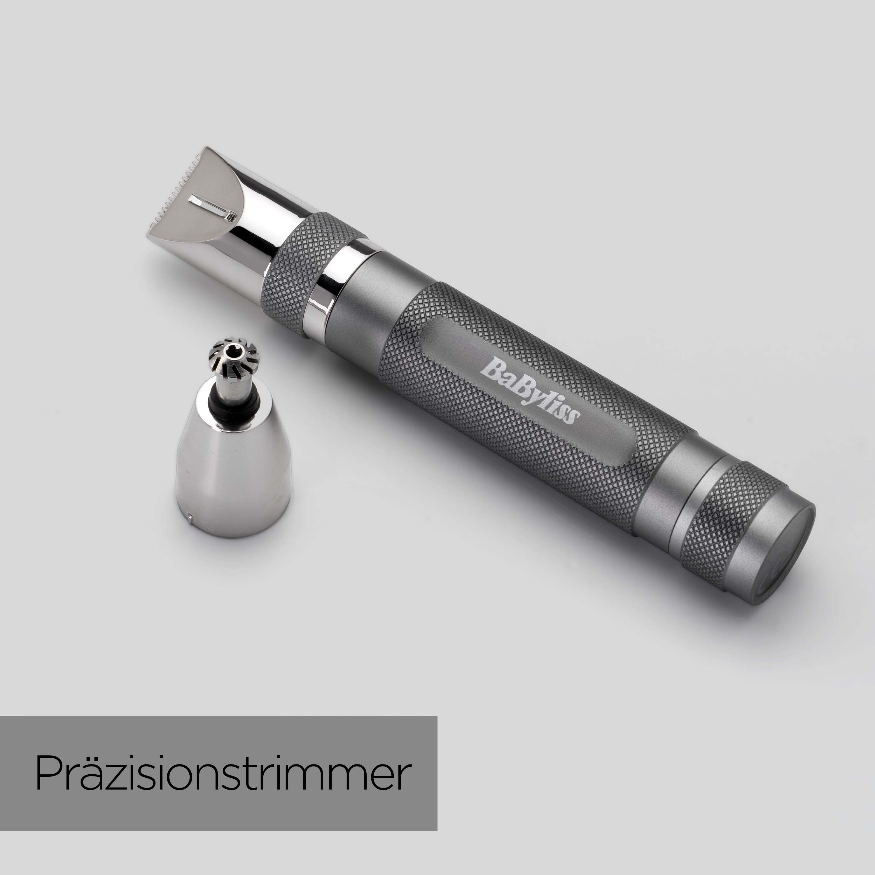 Ein grauer Babyliss-Präzisionstrimmer mit abnehmbarem Kopf und einem weiteren Kopfteil, alles auf hellgrauer Oberfläche.
