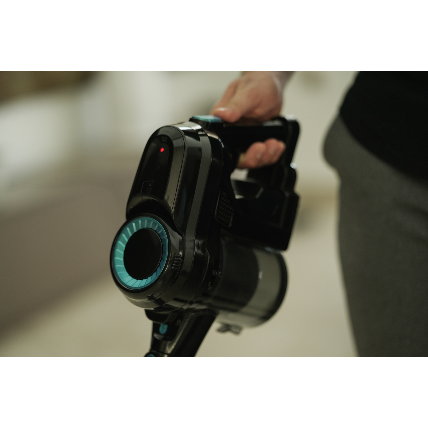 A person holds a black cordless vacuum cleaner. The vacuum has a blue and black design with a red light illuminated.