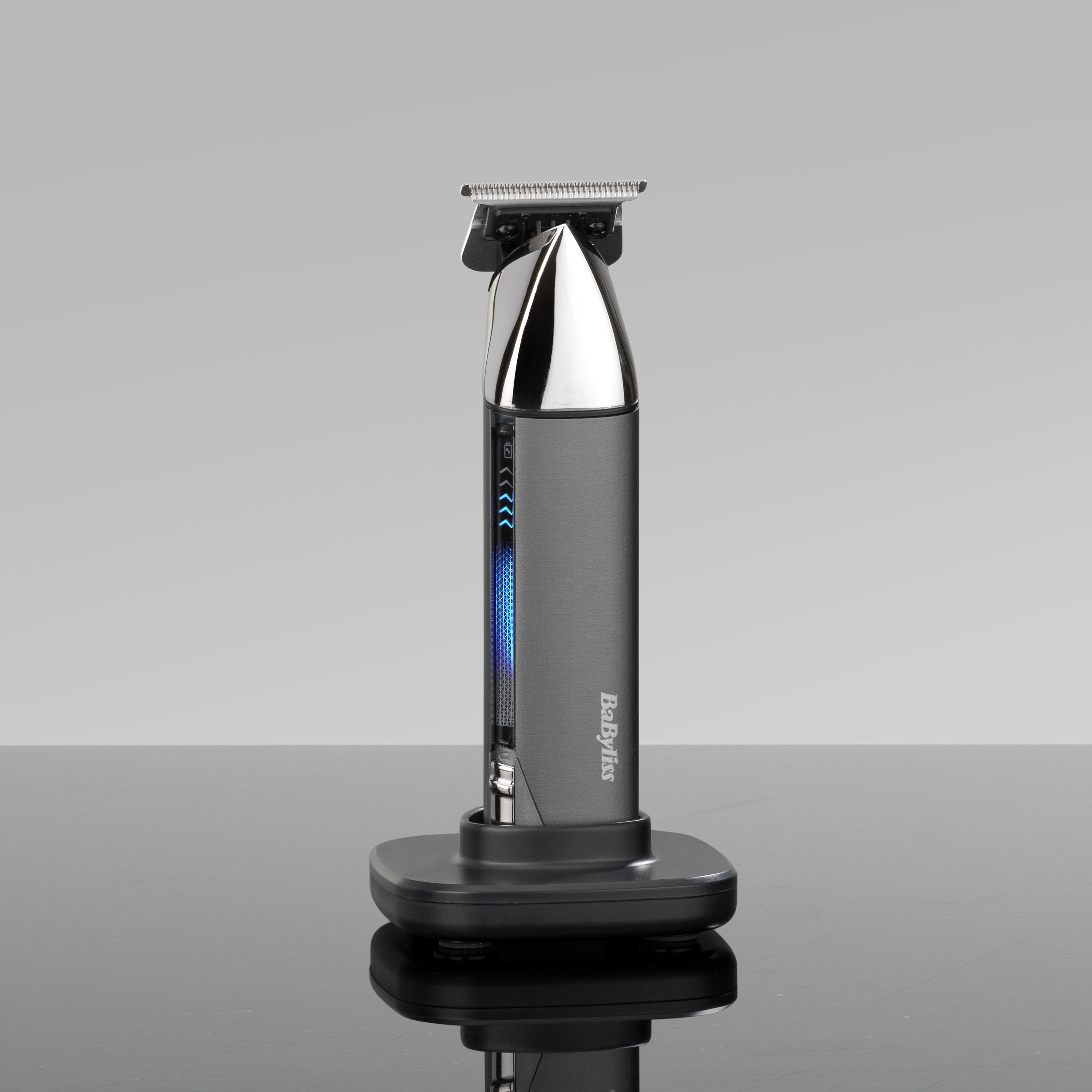 Ein Babyliss-Bartschneider steht aufrecht auf einer Ladestation. Er ist grau und silber, mit einer blauen Lichtanzeige.