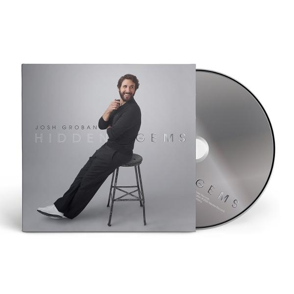 Josh Groban Album 'Hidden Gems'. Groban sitzt auf einem Hocker, neben der CD. Er trägt schwarze Kleidung und lächelt.