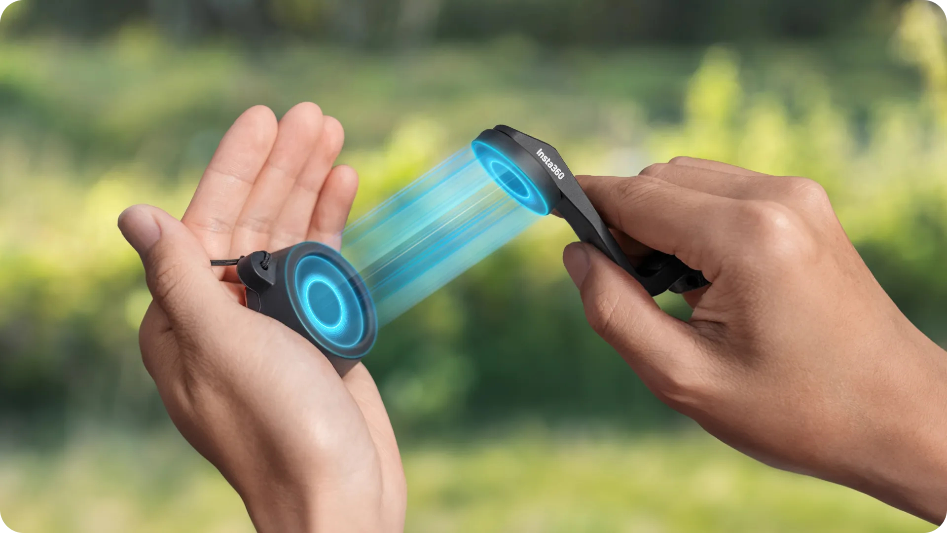 Hände halten ein schwarzes Insta360-Gerät mit blauem Strahl. Der Hintergrund ist verschwommenes grünes Laub.