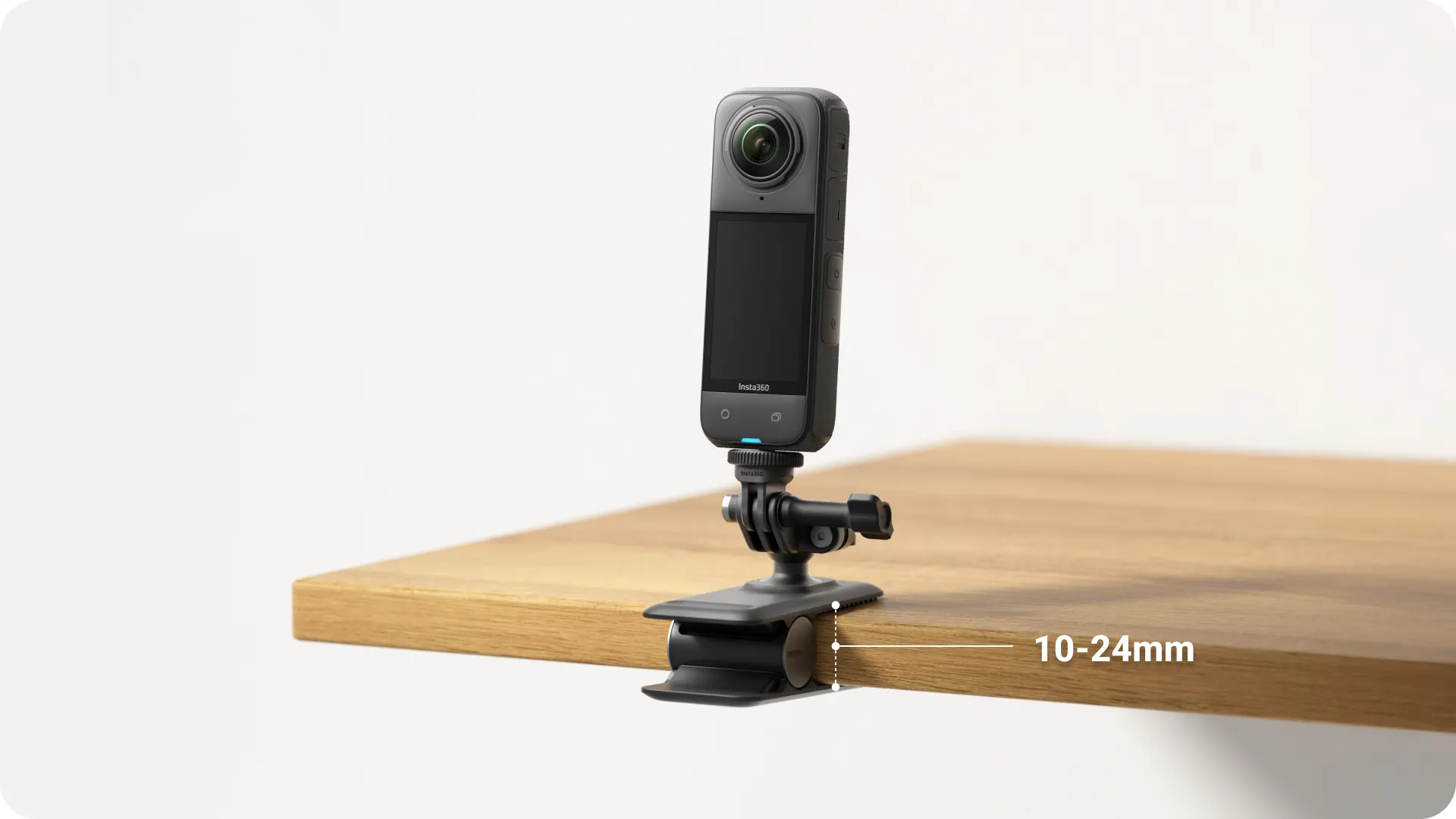 Eine schwarze Insta360-Kamera ist an einem schwarzen Clip befestigt, der an der Kante eines Holztisches befestigt ist. Der Hintergrund ist weiß.