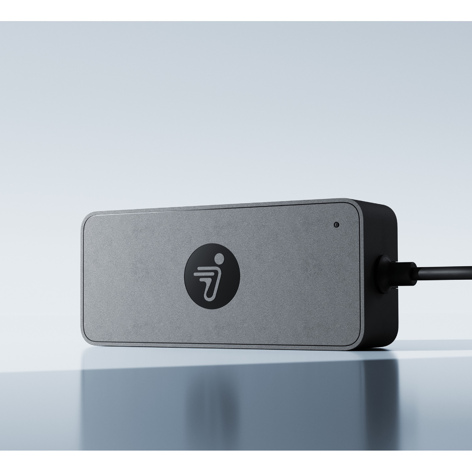 Grijs rechthoekig apparaat met zwart logo en kabel, op reflecterend oppervlak tegen witte achtergrond.