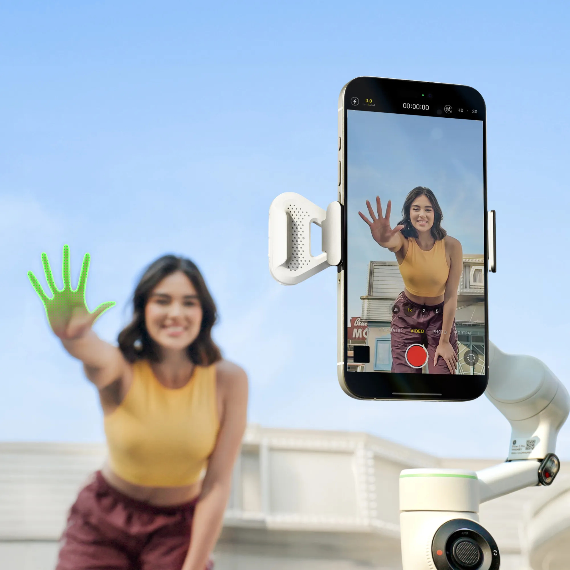 Eine Frau hält ihre Hand vor ein Telefon. Das Telefon befindet sich auf einem weißen Gimbal vor blauem Himmel. Das Telefon nimmt Video auf.