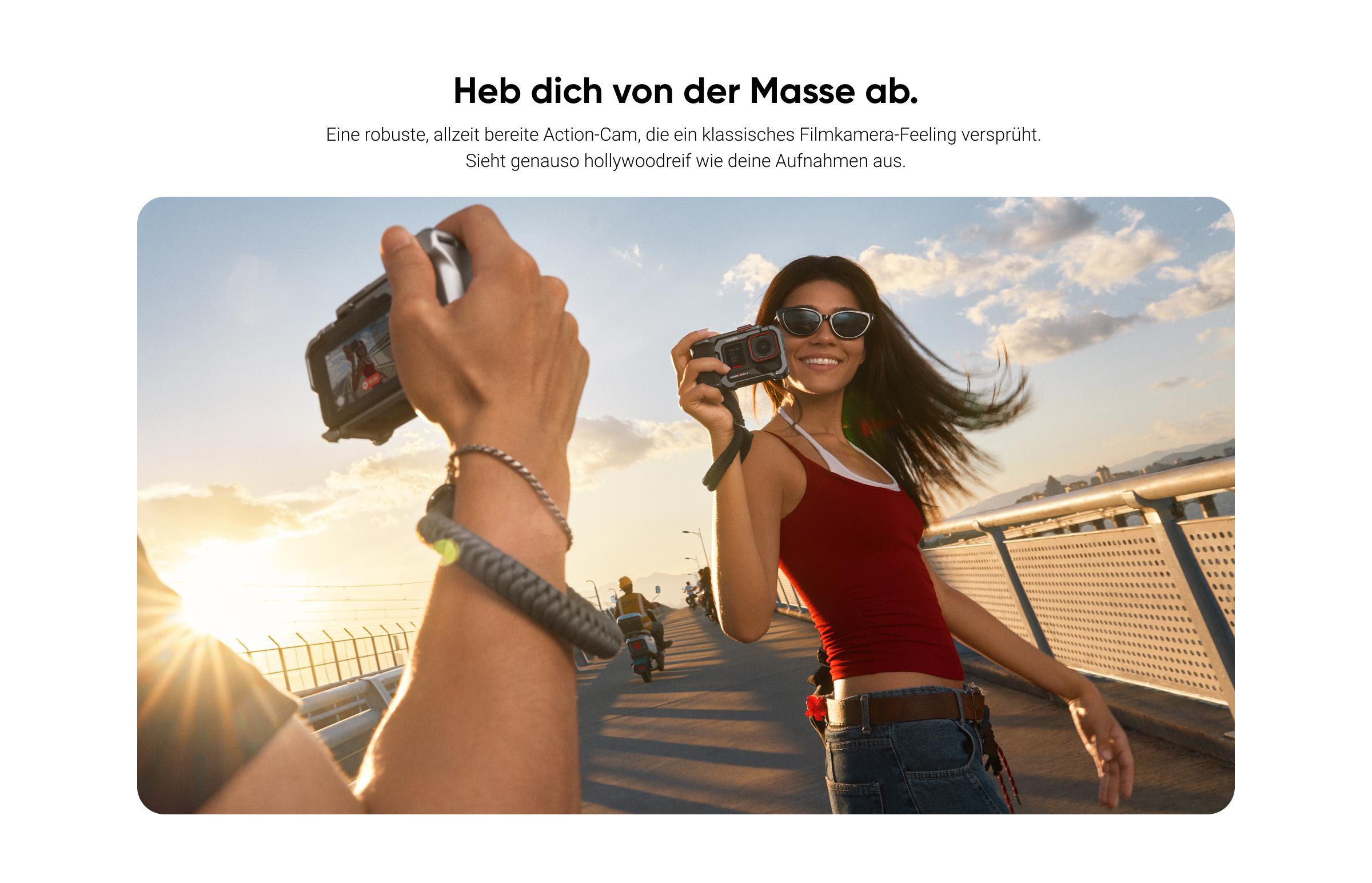 Eine Frau hält eine Kamera und lächelt. Eine Hand mit Armband hält eine andere. Menschen auf Rollern sind im Hintergrund.
