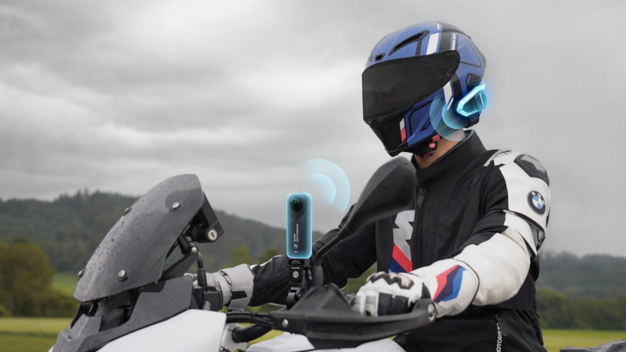 Eine Person auf einem Motorrad, mit Helm und Kommunikation sowie einer Kamera. Wolkenhimmel im Hintergrund.