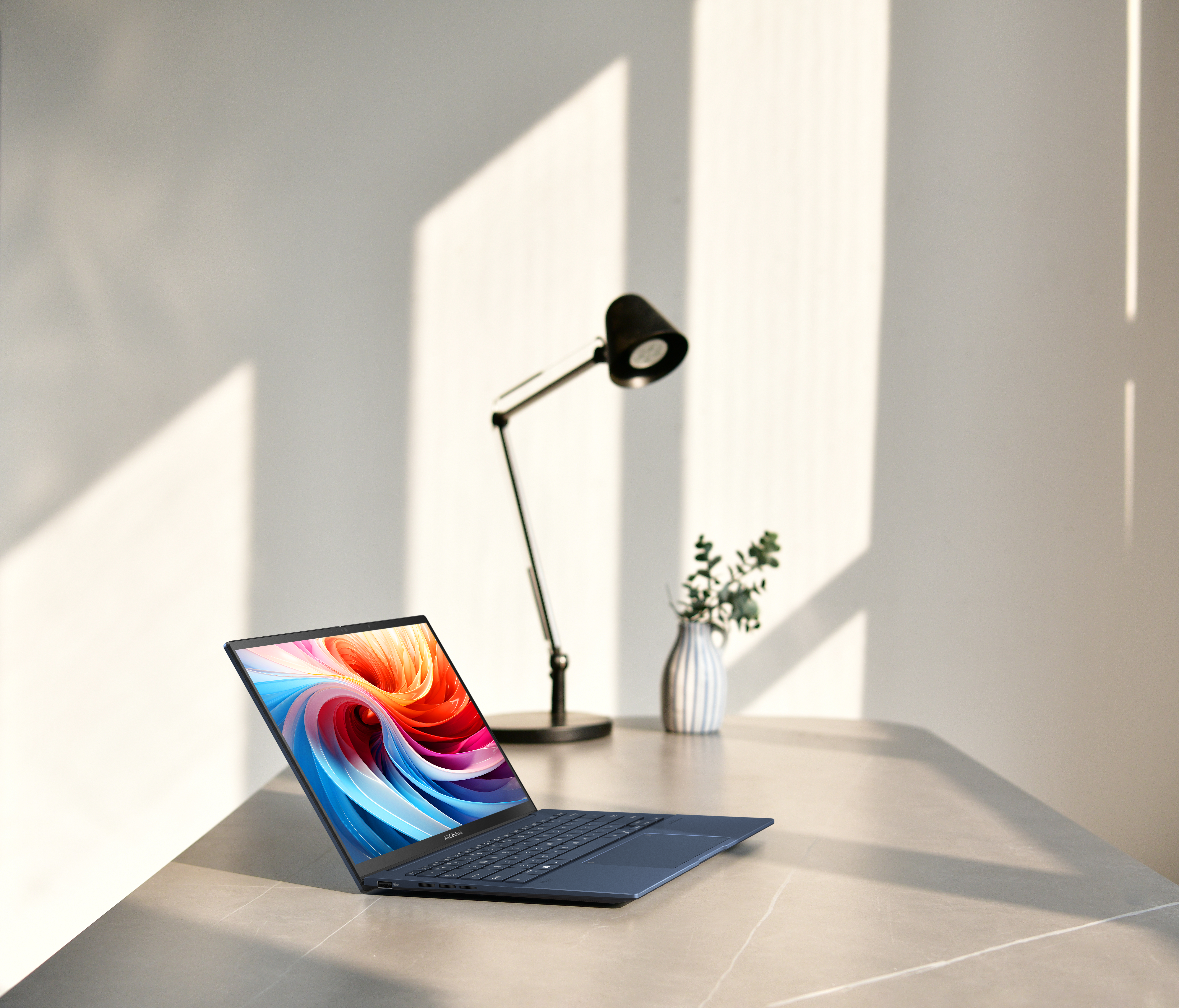 Laptop op tafel. Kleurrijk scherm, lamp en vaas op de achtergrond. Natuurlijk licht. Strak ontwerp.