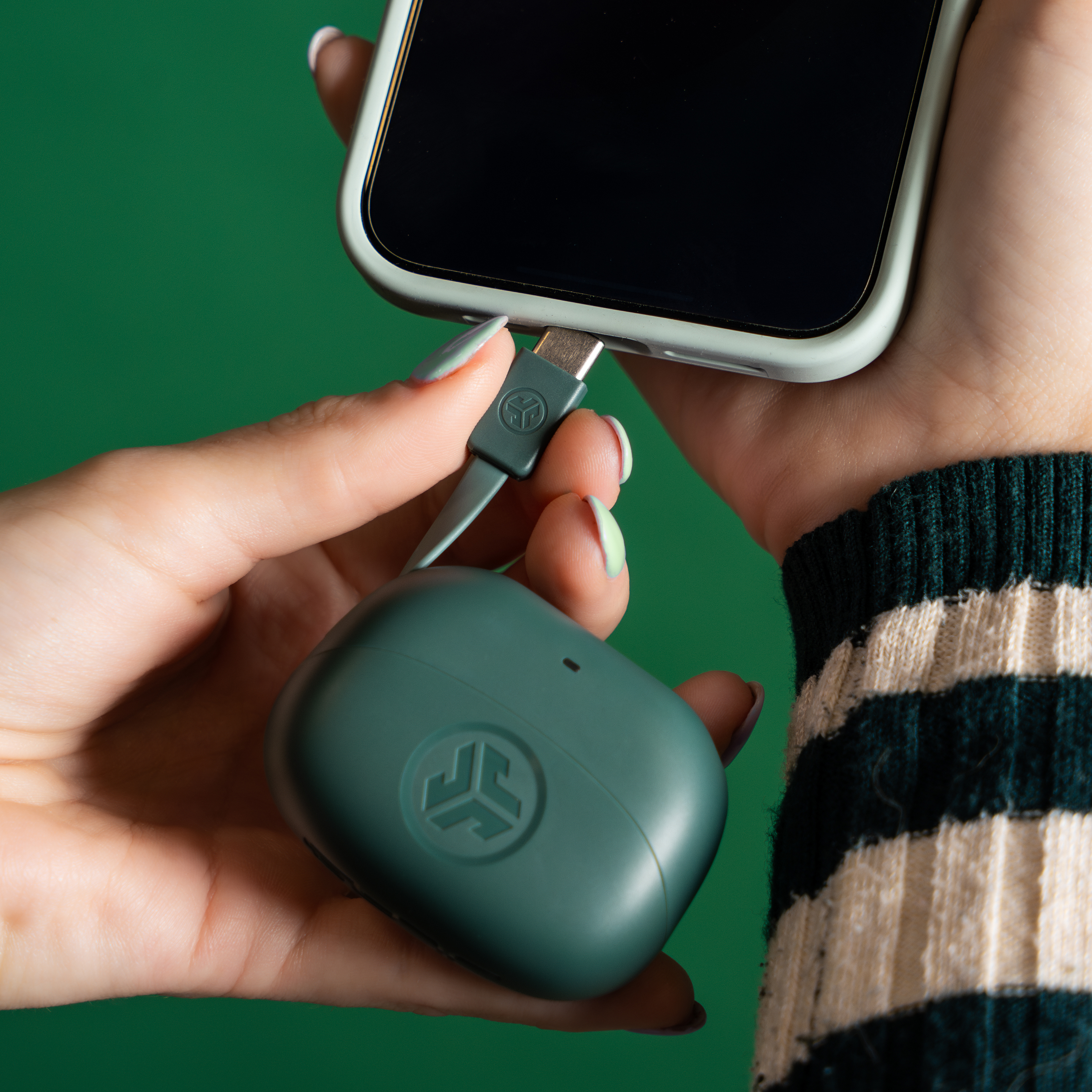 Hände halten Telefon und Kopfhörer-Etui, verbunden durch ein Kabel. Der Hintergrund ist grün.
