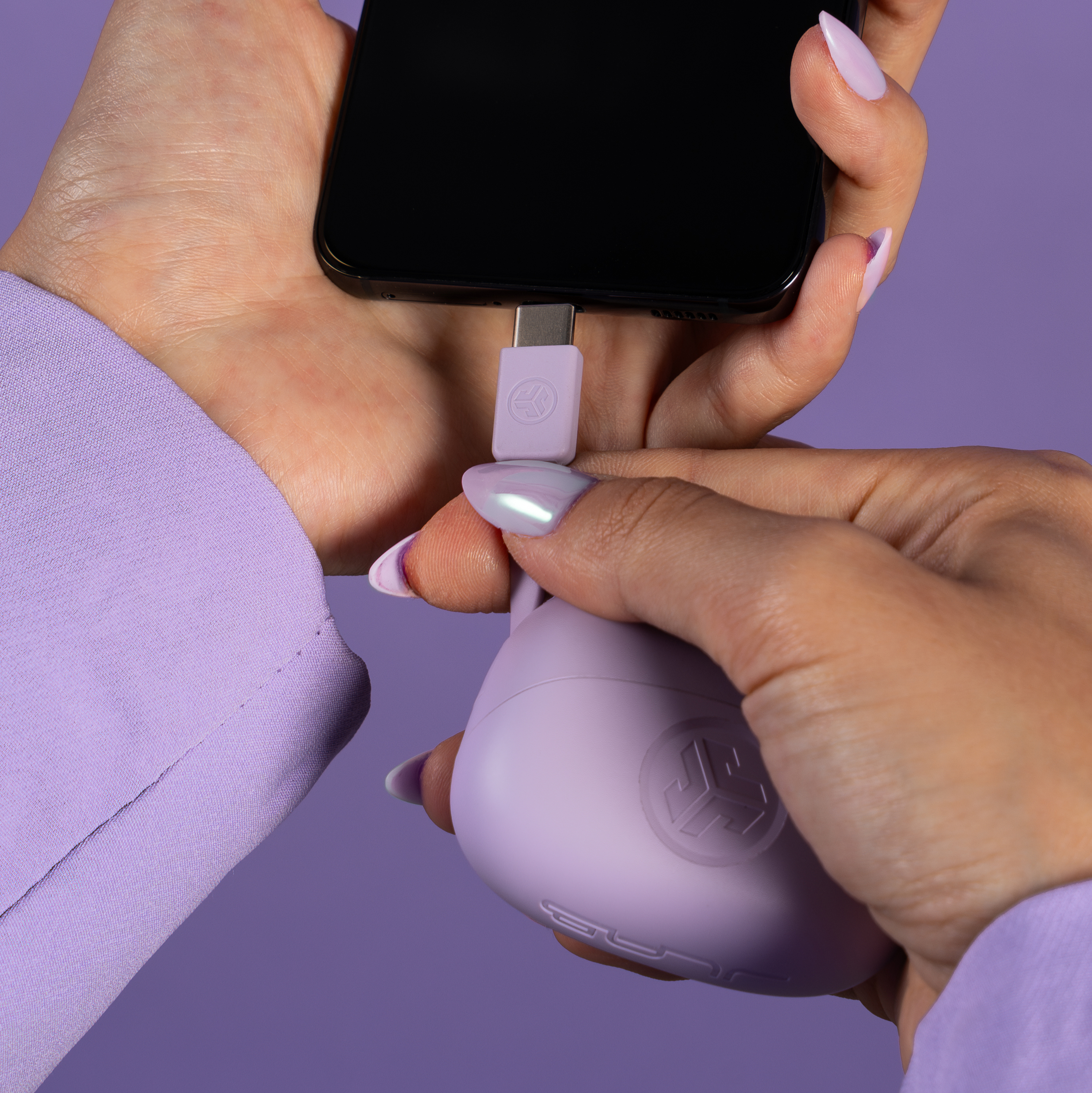Hände halten Telefon und Ladegerät. Ladegerät ist in das Telefon gesteckt. Lila Hintergrund und Kleidung sind sichtbar.