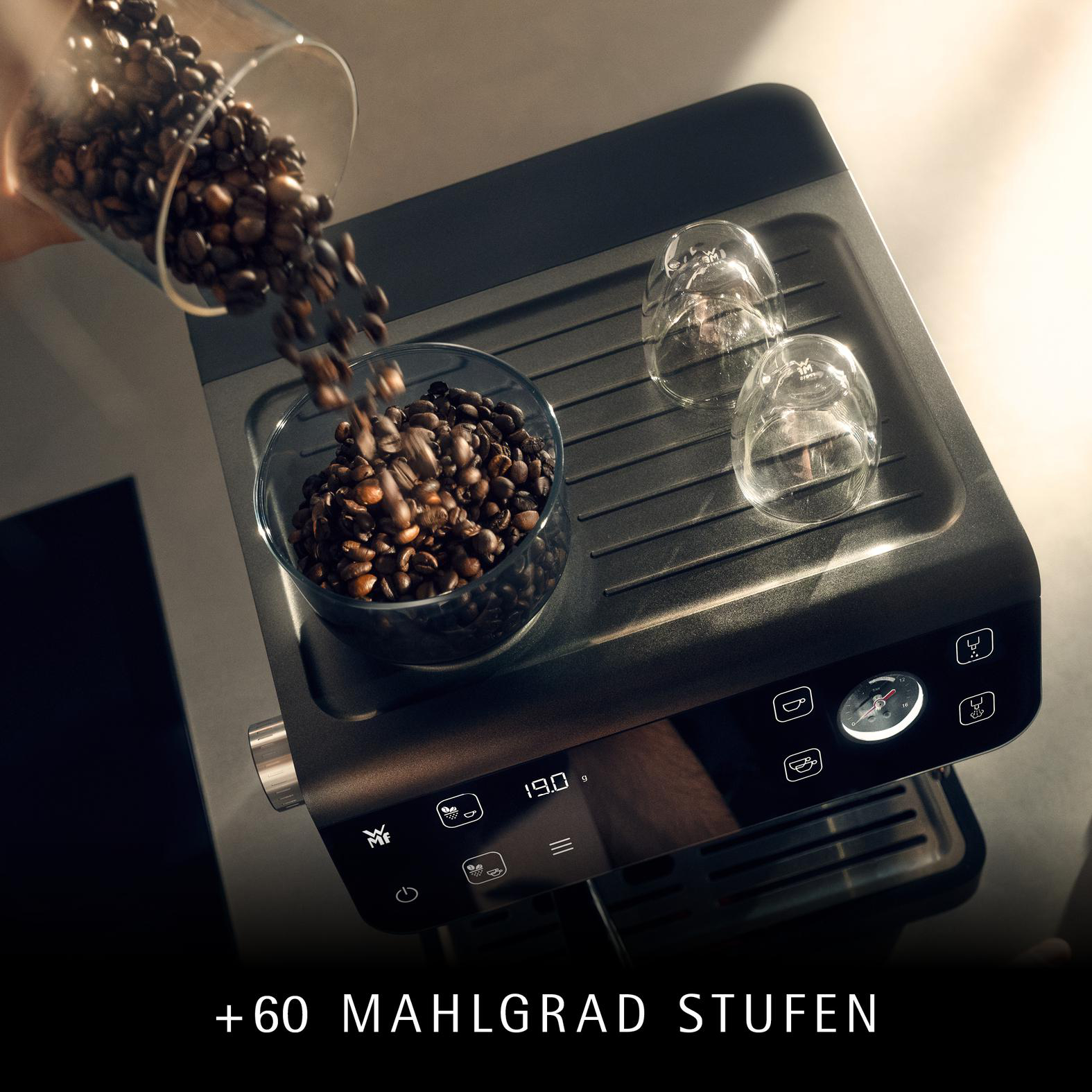 Kaffeebohnen gießen in eine Glasschale auf einer Kaffeemaschine. Zwei Gläser befinden sich auf der Maschine.