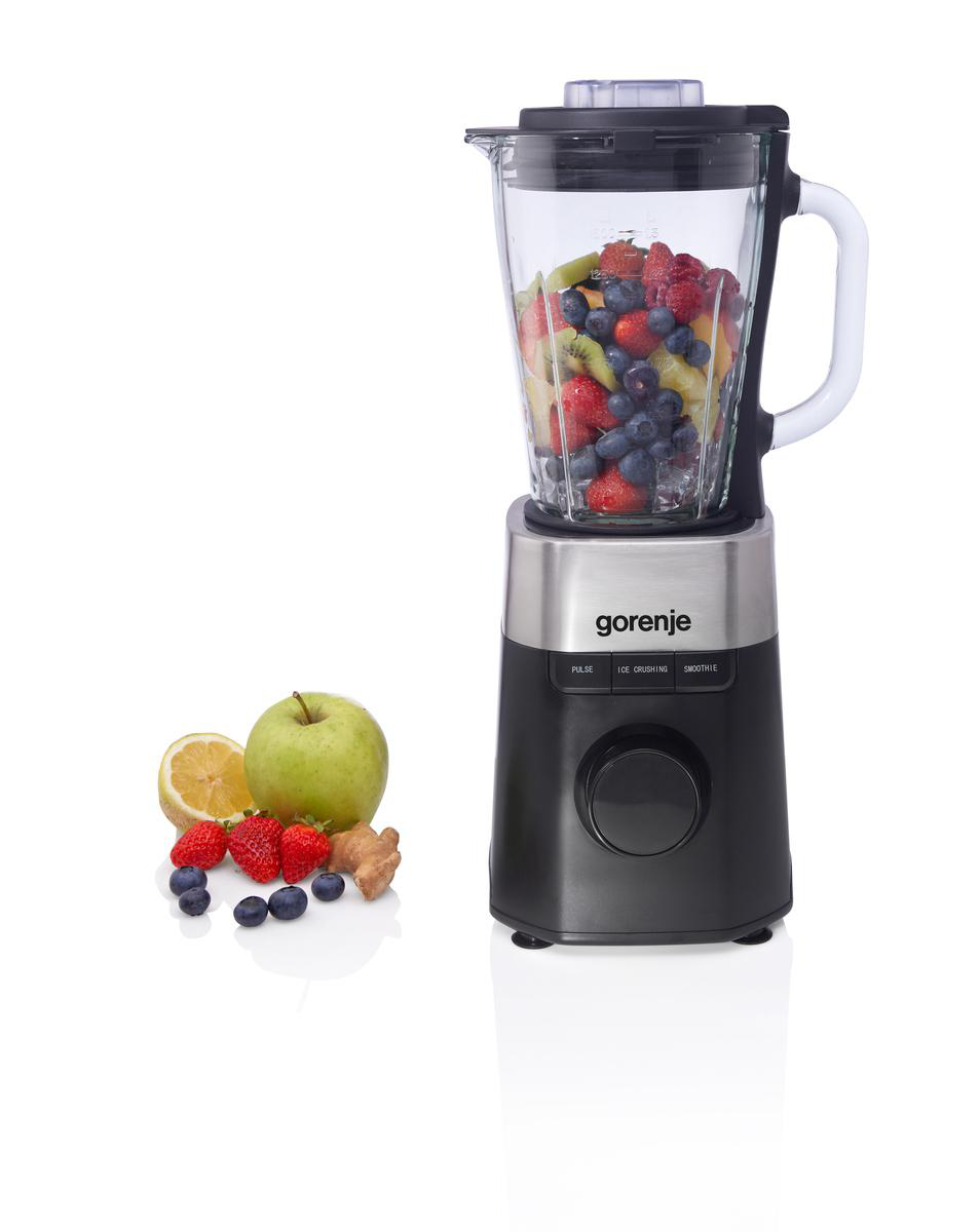 Mixer mit Früchten wie Erdbeeren, Blaubeeren, Kiwi und Pfirsichen. Daneben Zitrone, Apfel, Ingwer und Beeren.