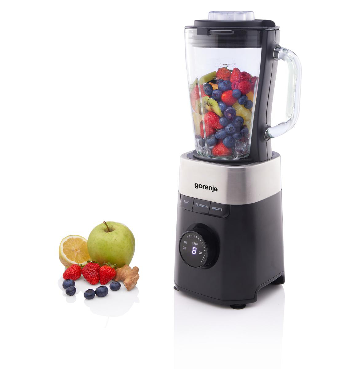 Ein Mixer mit Früchten steht neben einem Apfel, einer Zitrone, Erdbeeren, Blaubeeren und Ingwer.